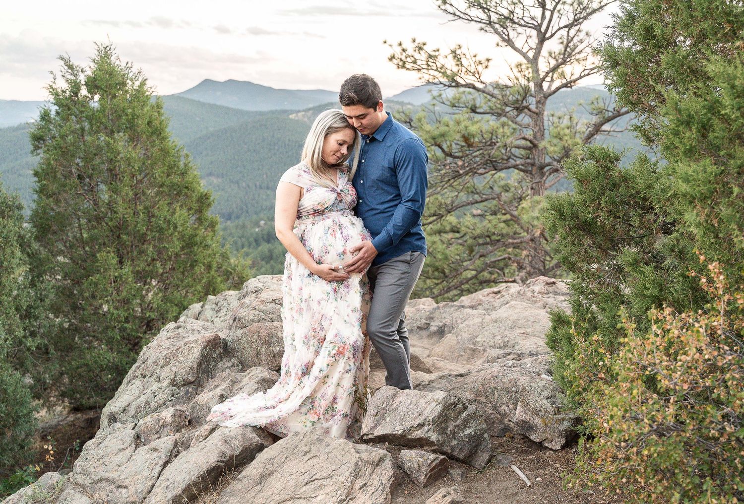 A couple shares a romantic moment posing together on a rocky mountain overlook with scenic views in the background.