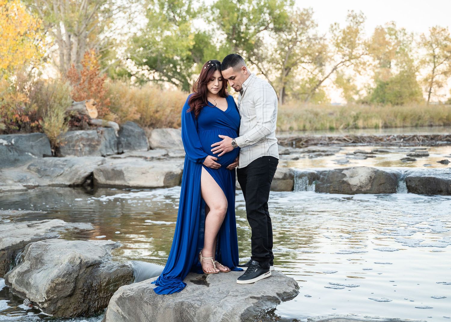 Maternity photography session on rocky outcrop by water featuring elegant blue gown.