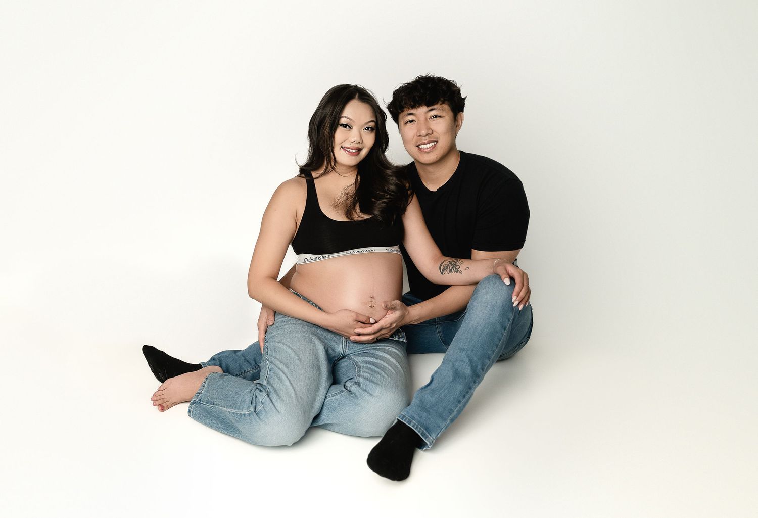 Modern minimalist maternity studio session with casual denim styling on white background.