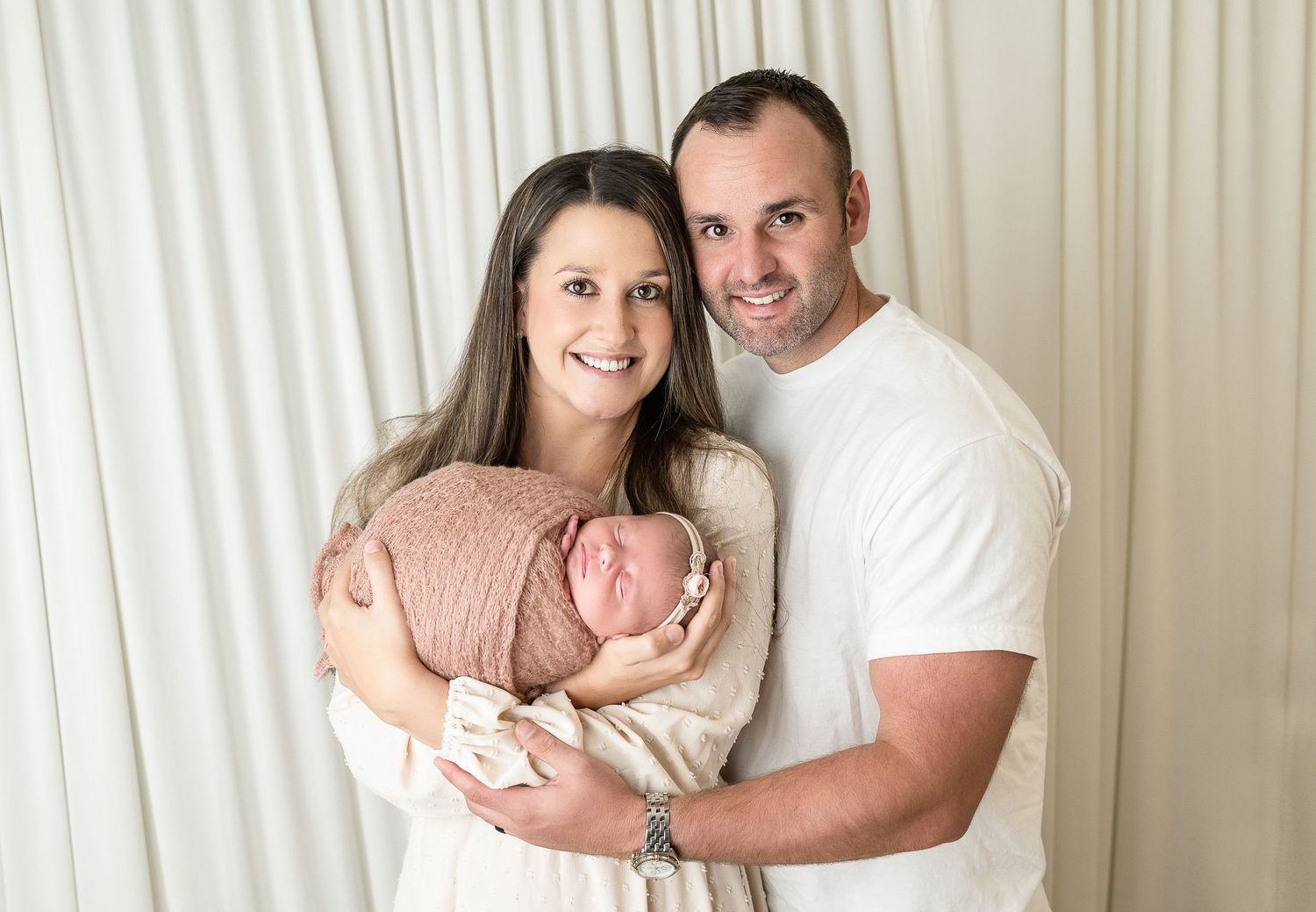A series of family portrait photos with parents and newborn baby in white and neutral tones against studio backdrop.