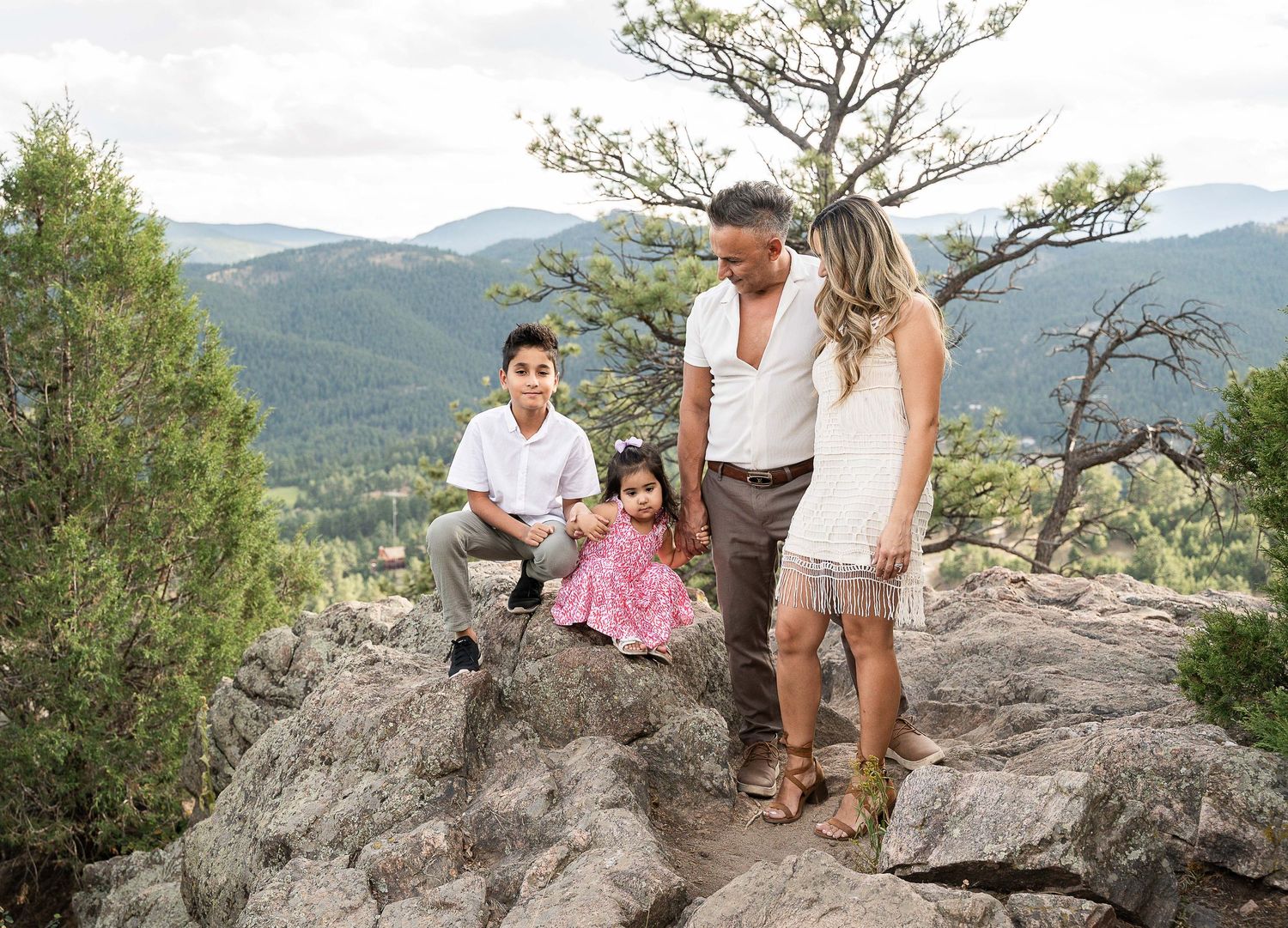Family explores scenic mountain overlook at Mount Falcon Park with mountains and trees in the background. Family session in Denver, Colorado