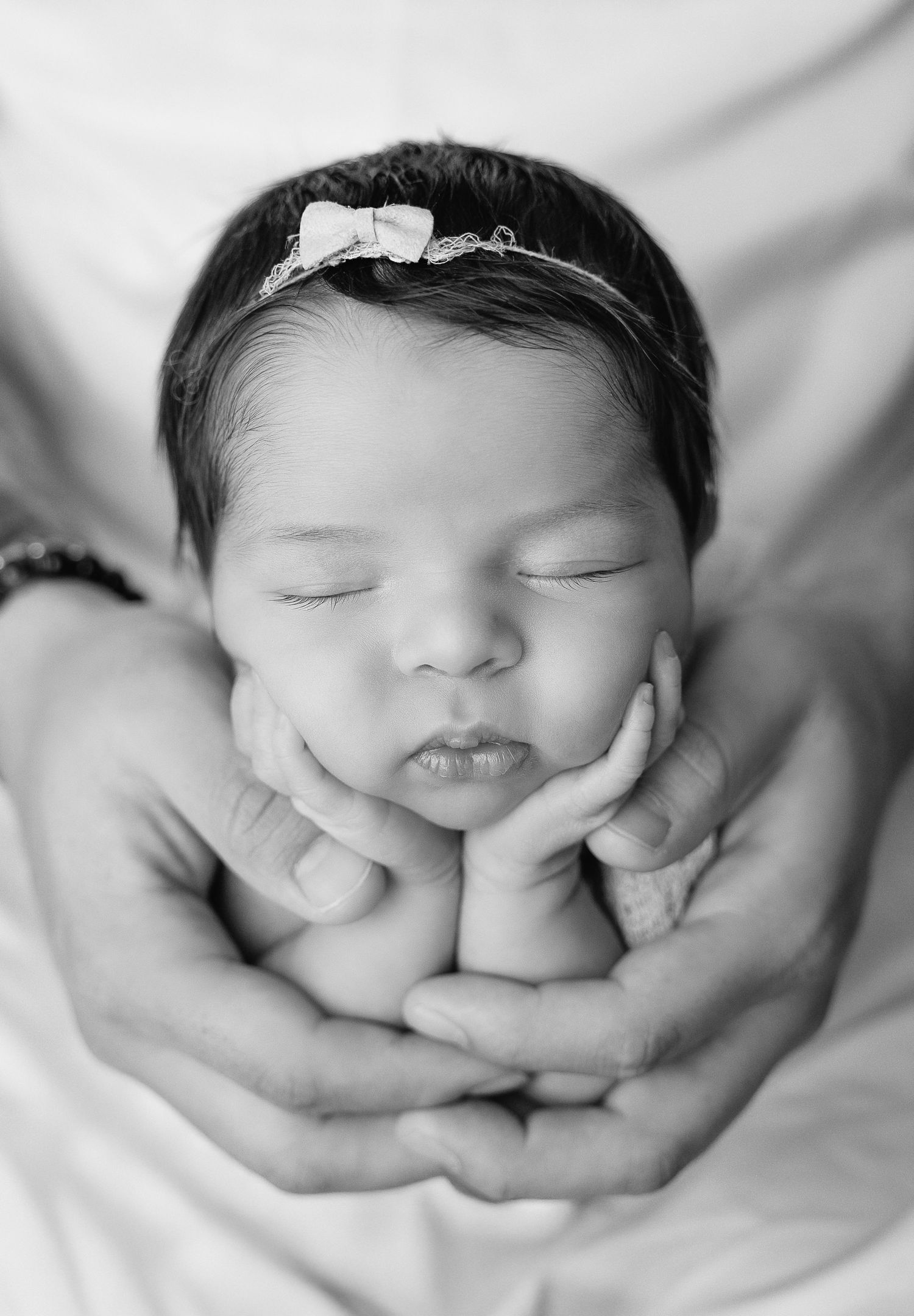 Black and white portrait of sleeping newborn cradled tenderly in hands.