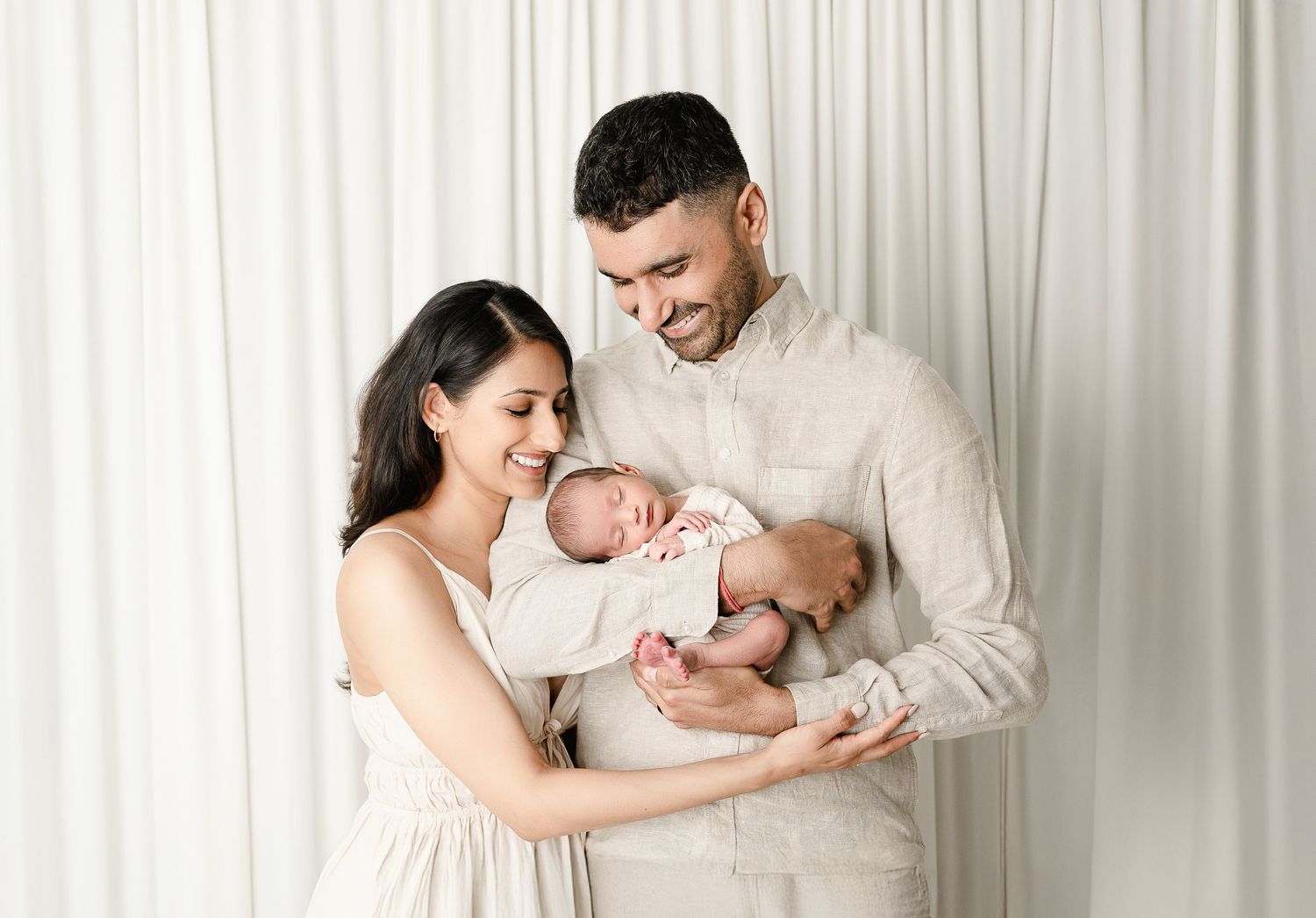 A heartwarming collection of family portraits showing tender moments with a newborn baby against a white curtain backdrop.