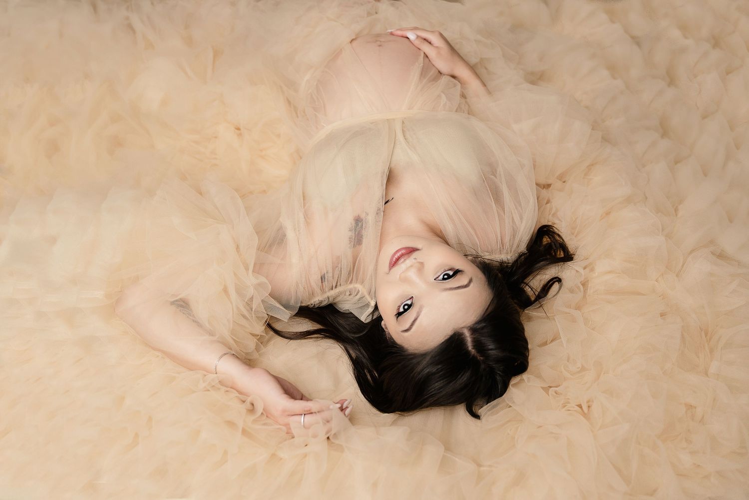 Artistic maternity portrait on cream carpet with soft, dreamy lighting.