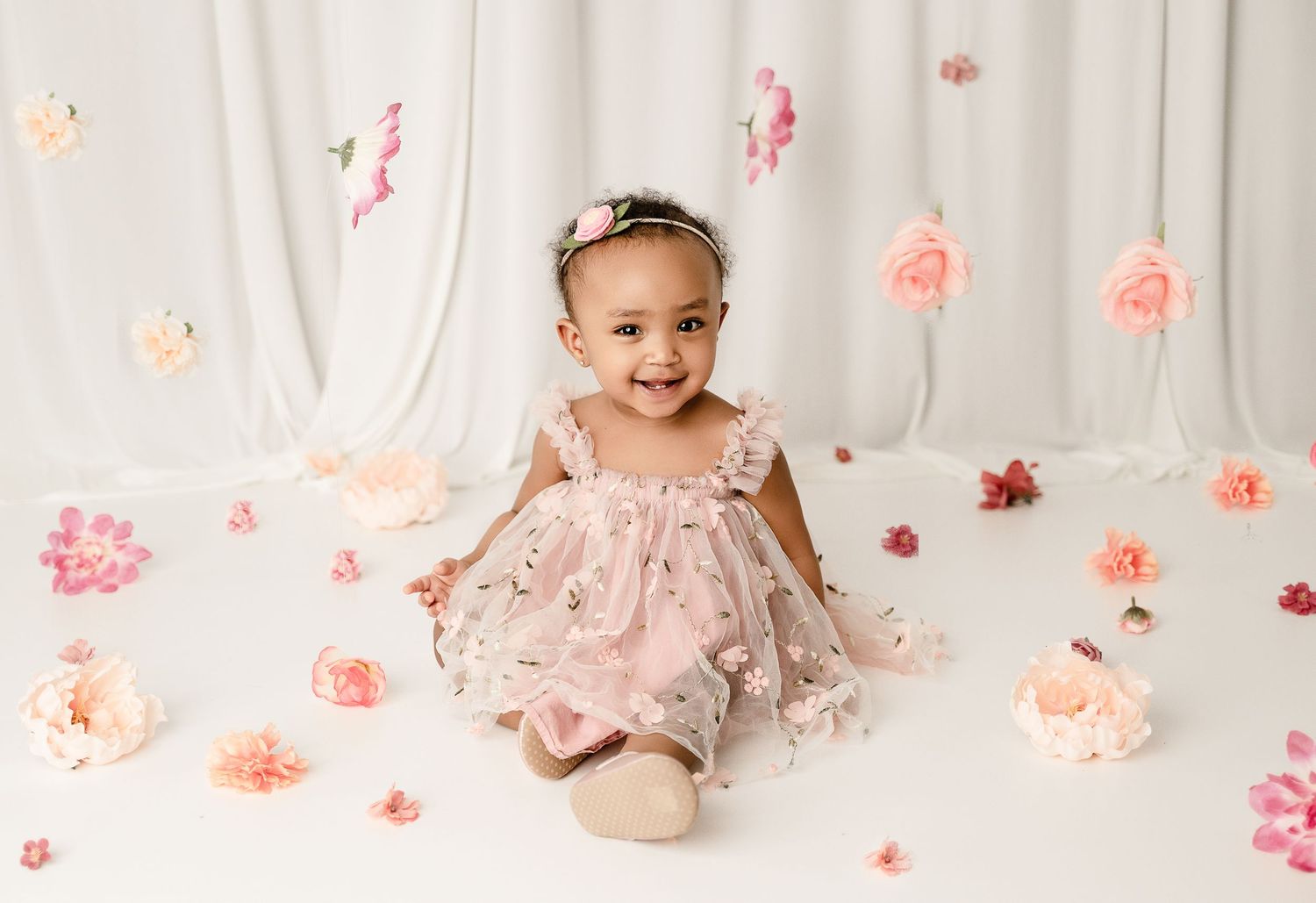 Floral themed first birthday setup with pink roses and white backdrop.