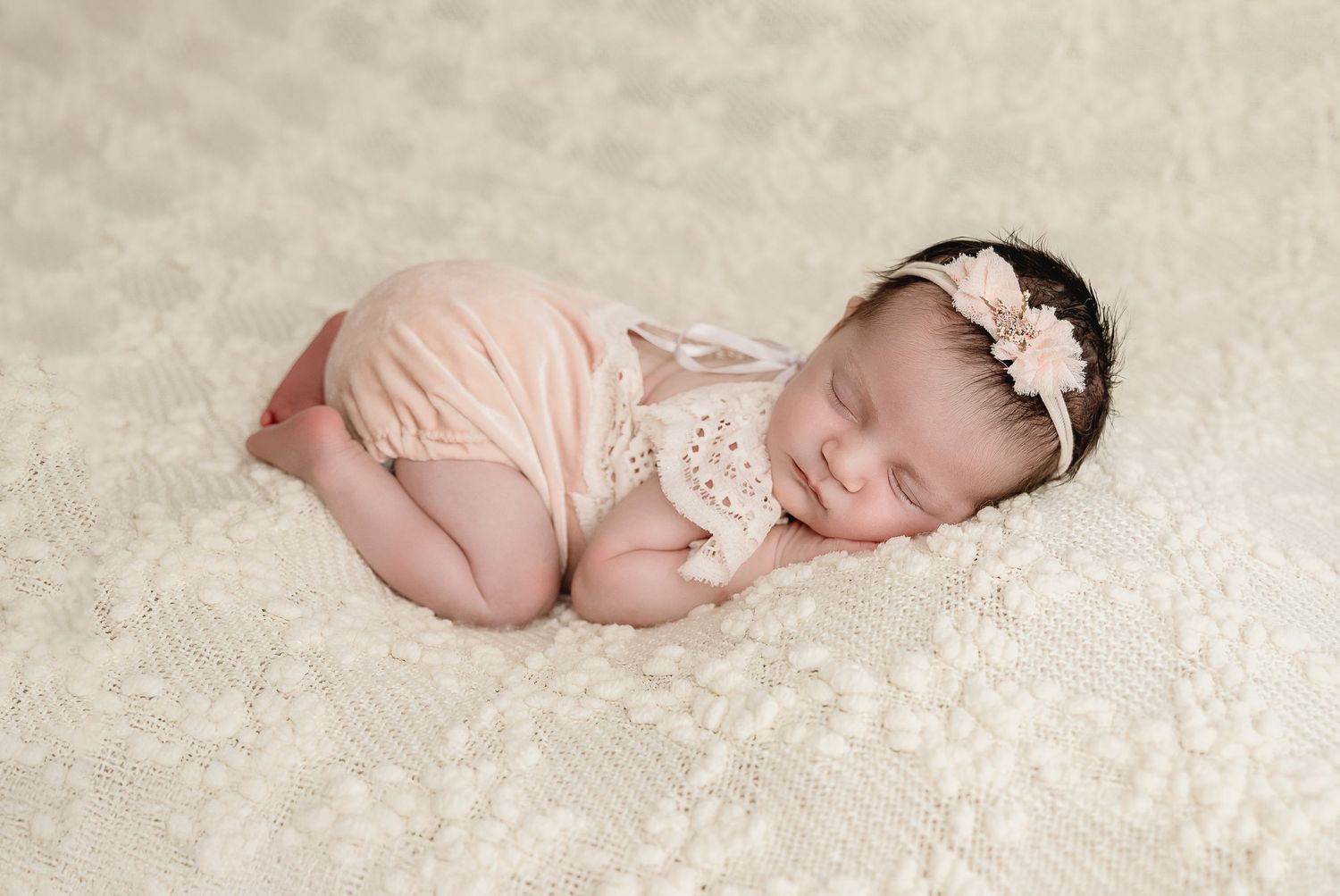 Sweet newborn photo session with delicate lace headband on ivory textured backdrop.