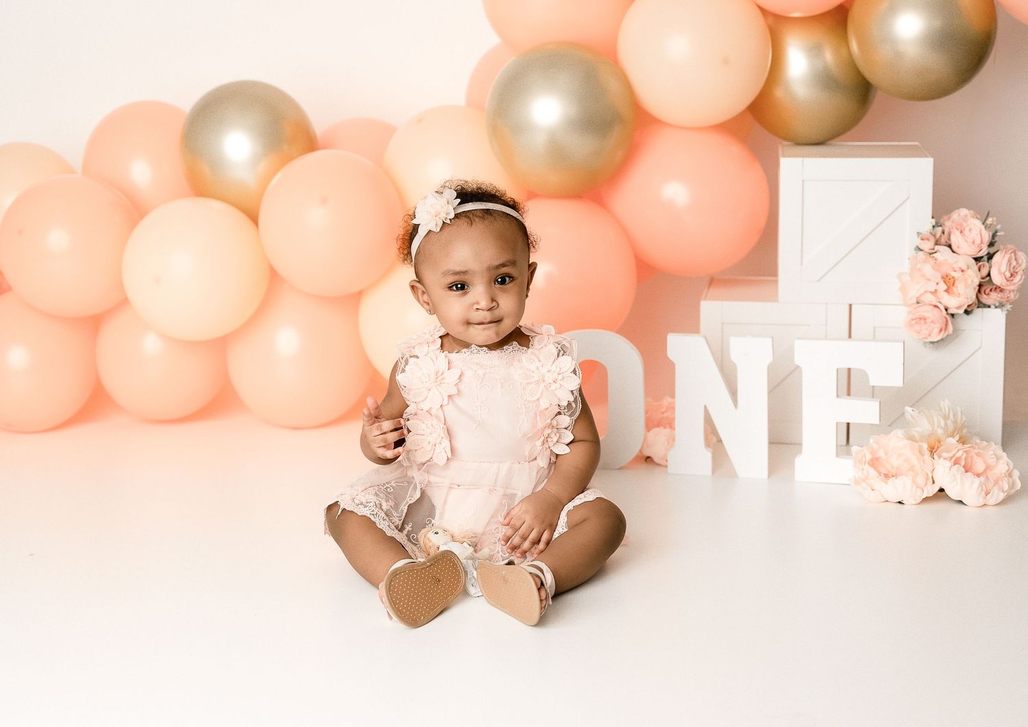 Peach and silver balloon arch with 'ONE' letter sign for first birthday celebration.