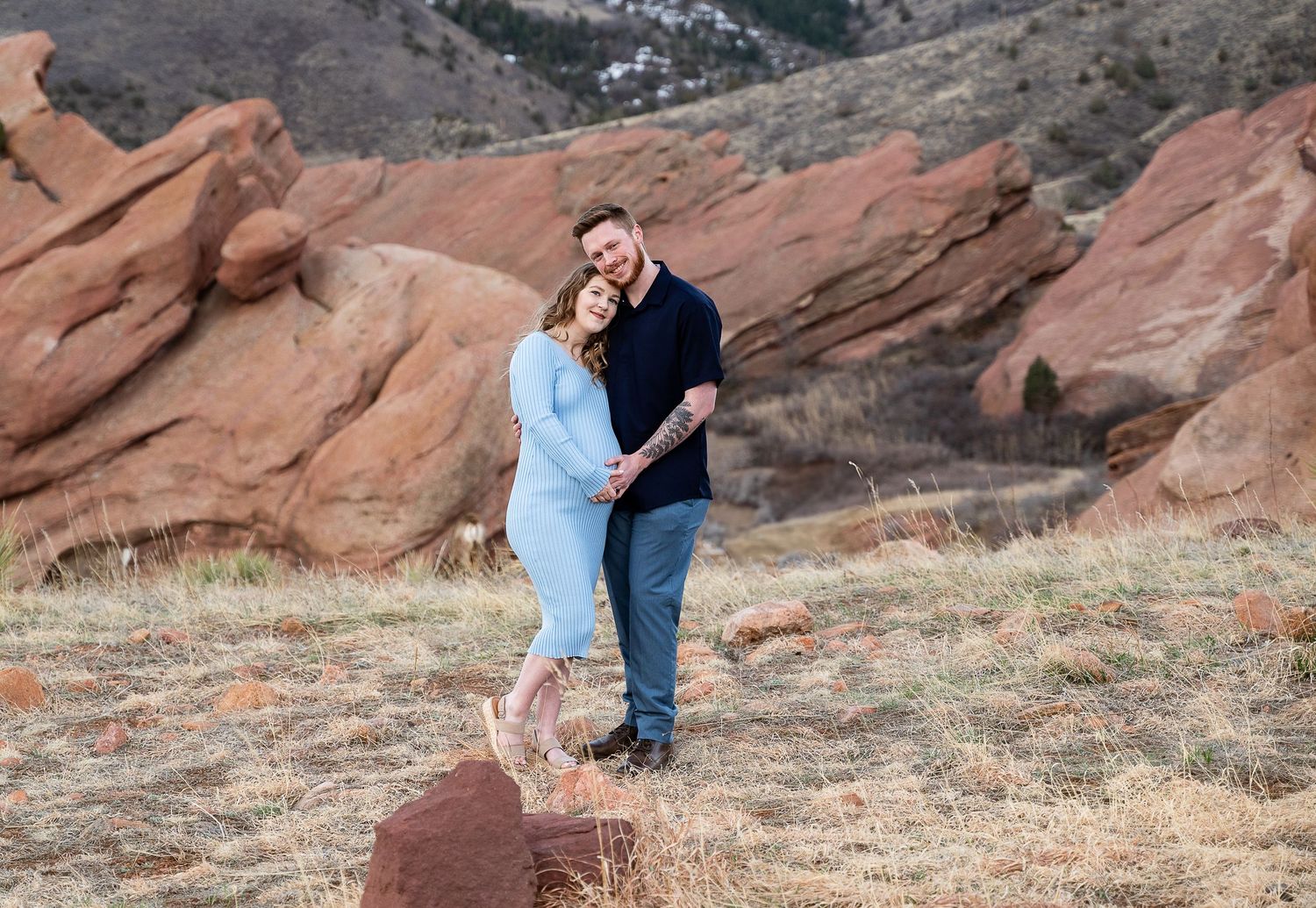 Two people embrace while standing among the iconic red rock formations at Red Rocks Park in Colorado.