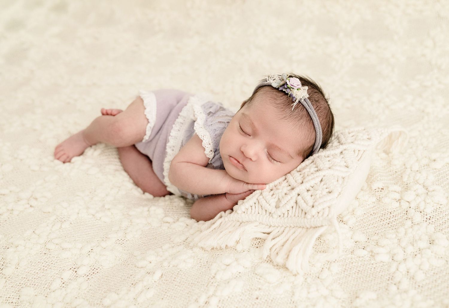 A sleeping newborn baby lies peacefully on soft cream-colored lace fabric in a professional portrait setting.