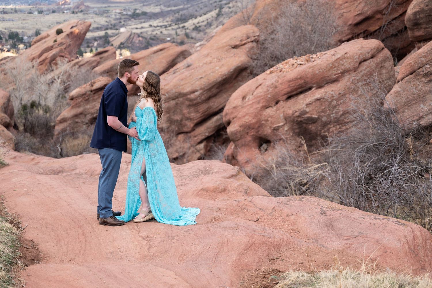 A couple shares an intimate moment against dramatic red rock formations.