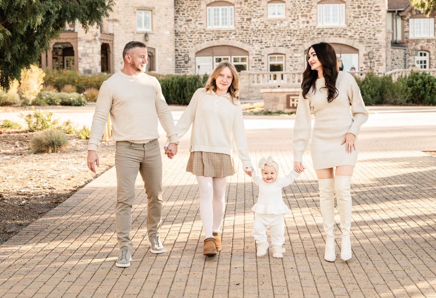 Family walking together and holding hands along a stone path outside a rustic building in warm sunlight.