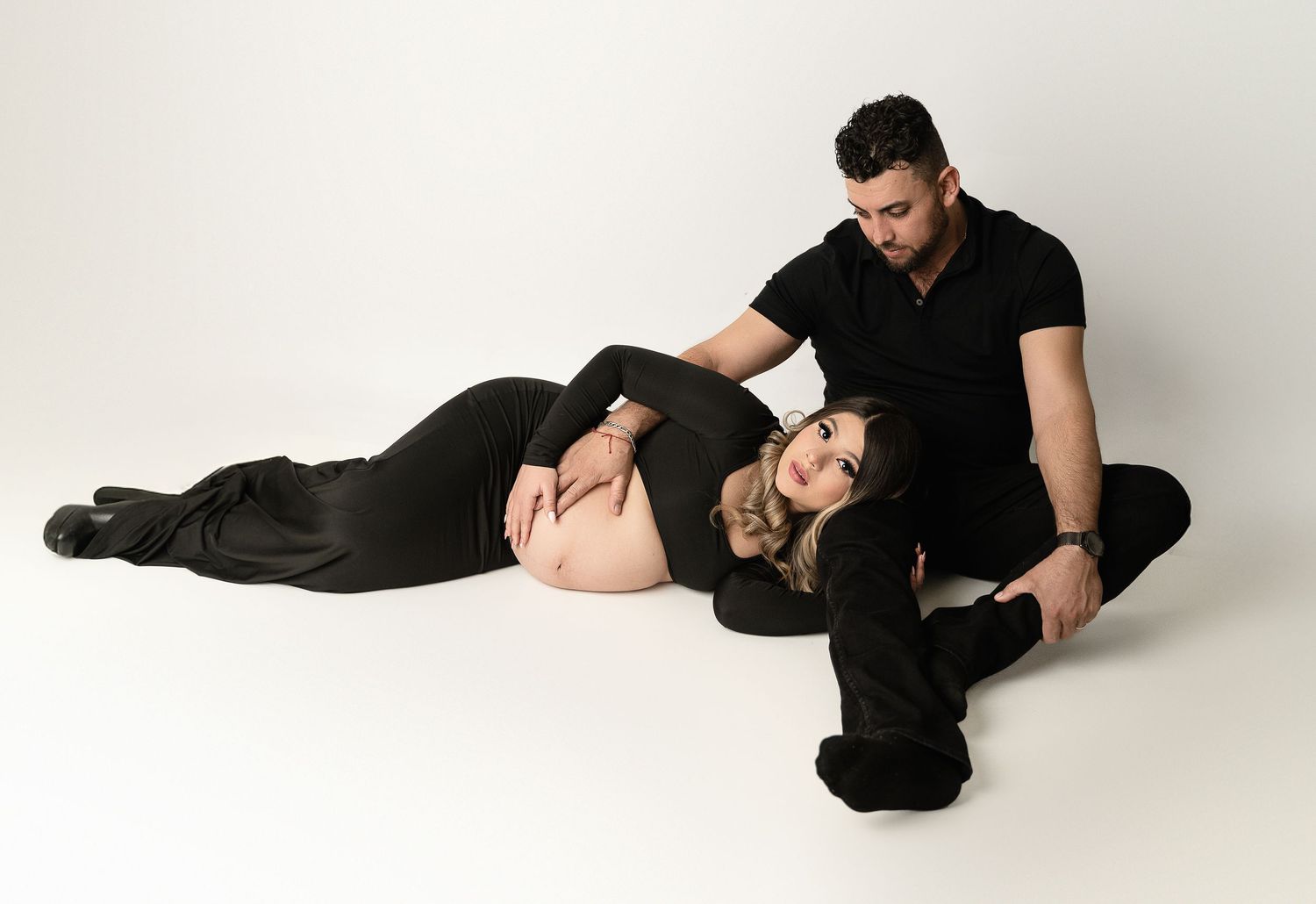 Intimate maternity photo session with couple in black outfits on white background.