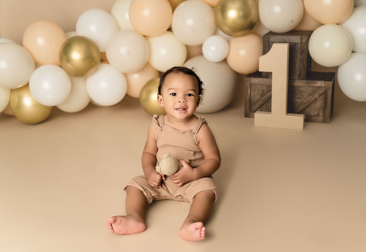 Milestone photography setup with gold and white balloons and number one decor on beige backdrop.