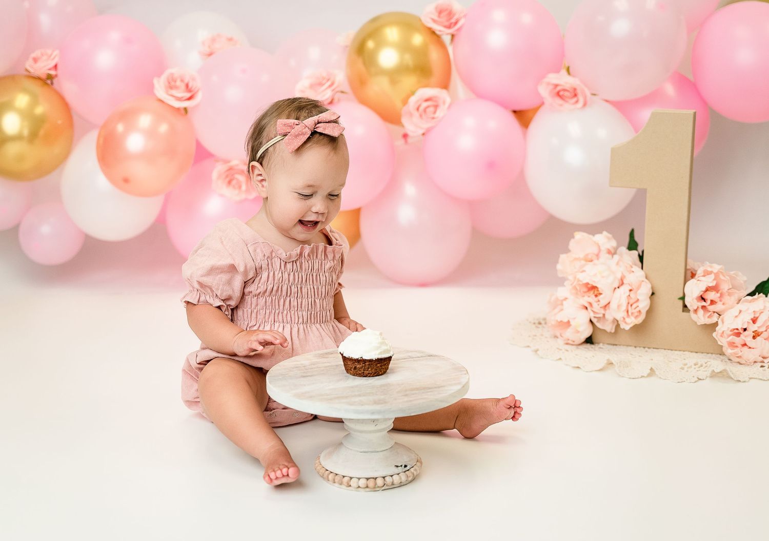 Pink themed cake smash session with gold balloons and floral decorations.