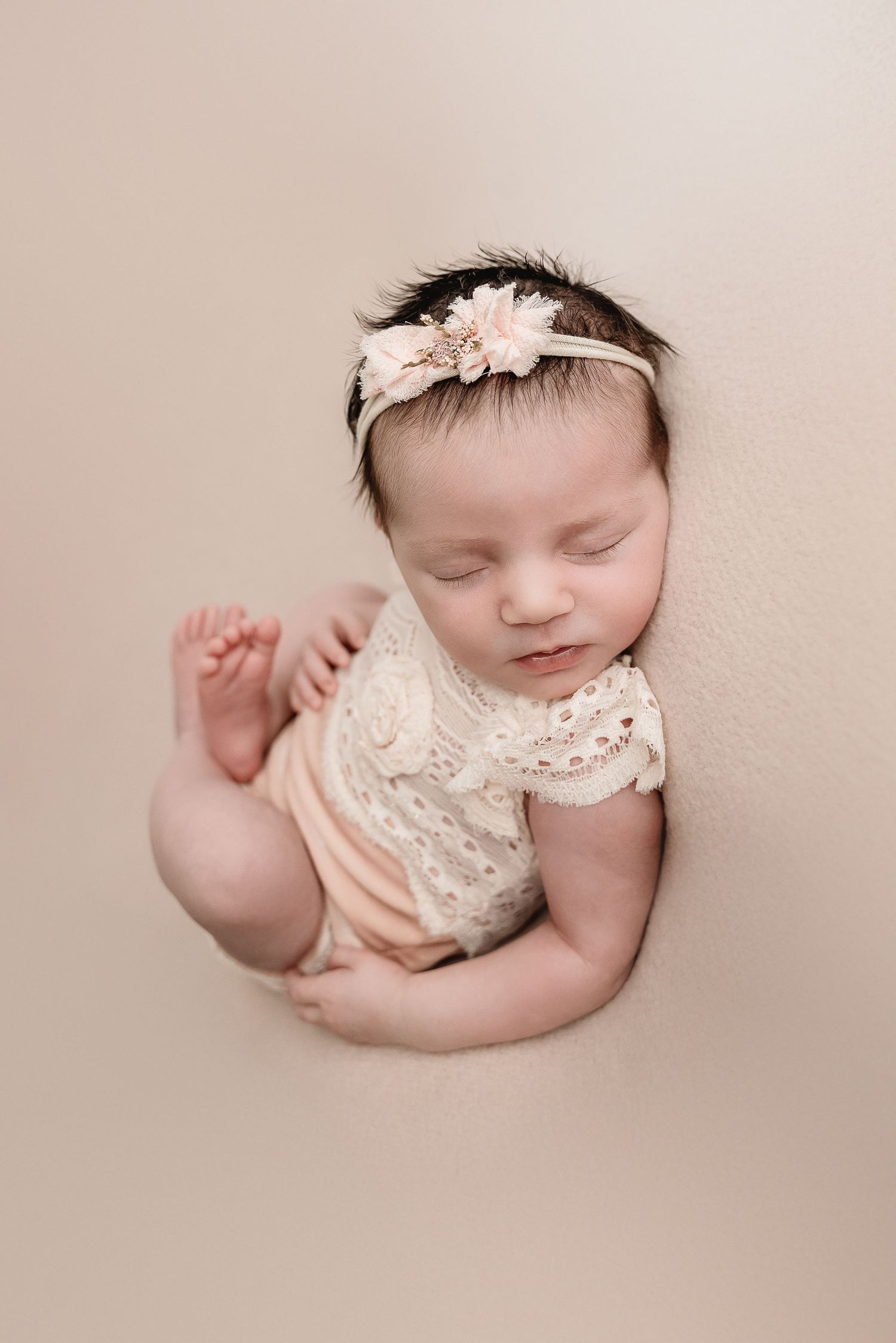 Artistic newborn portrait with lace outfit against neutral beige background.