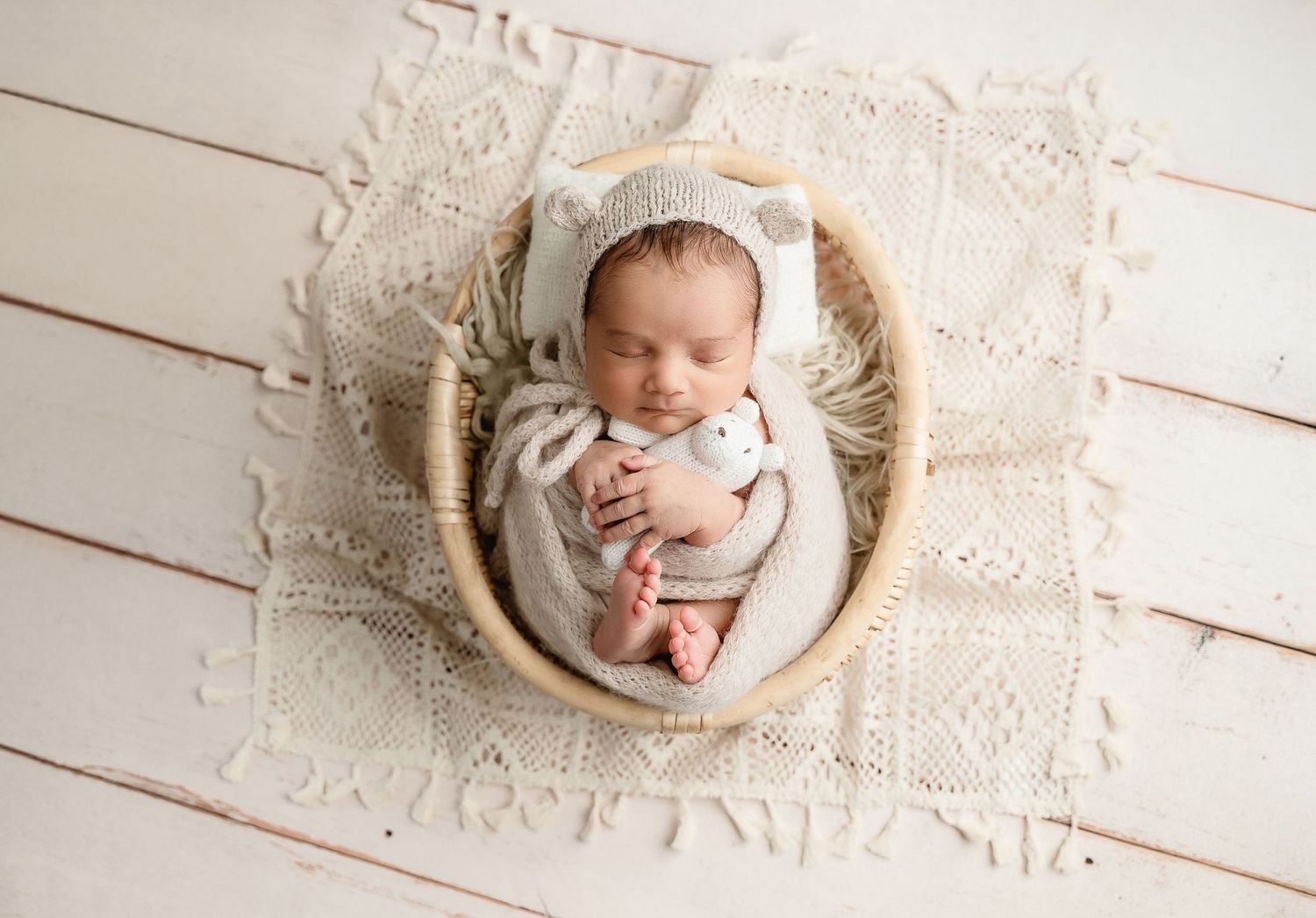 Sleeping newborn in white wrap posed in wooden bowl on lace blanket.