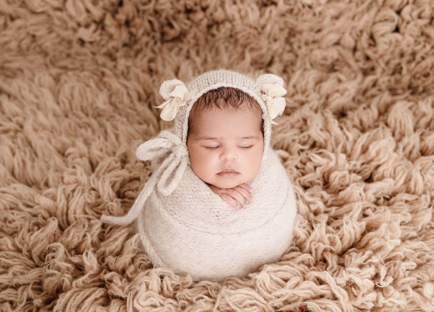 A series of sepia-toned newborn photography portraits showing a sleeping baby wrapped in soft white fabric on textured carpet.