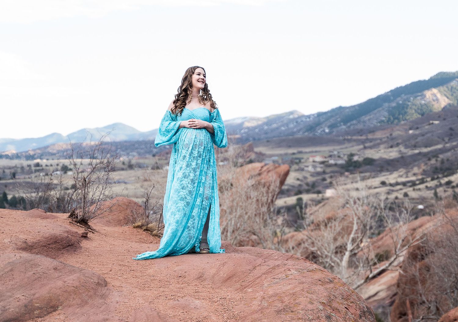 A maternity portrait showcases a woman in turquoise against a mountainous backdrop.