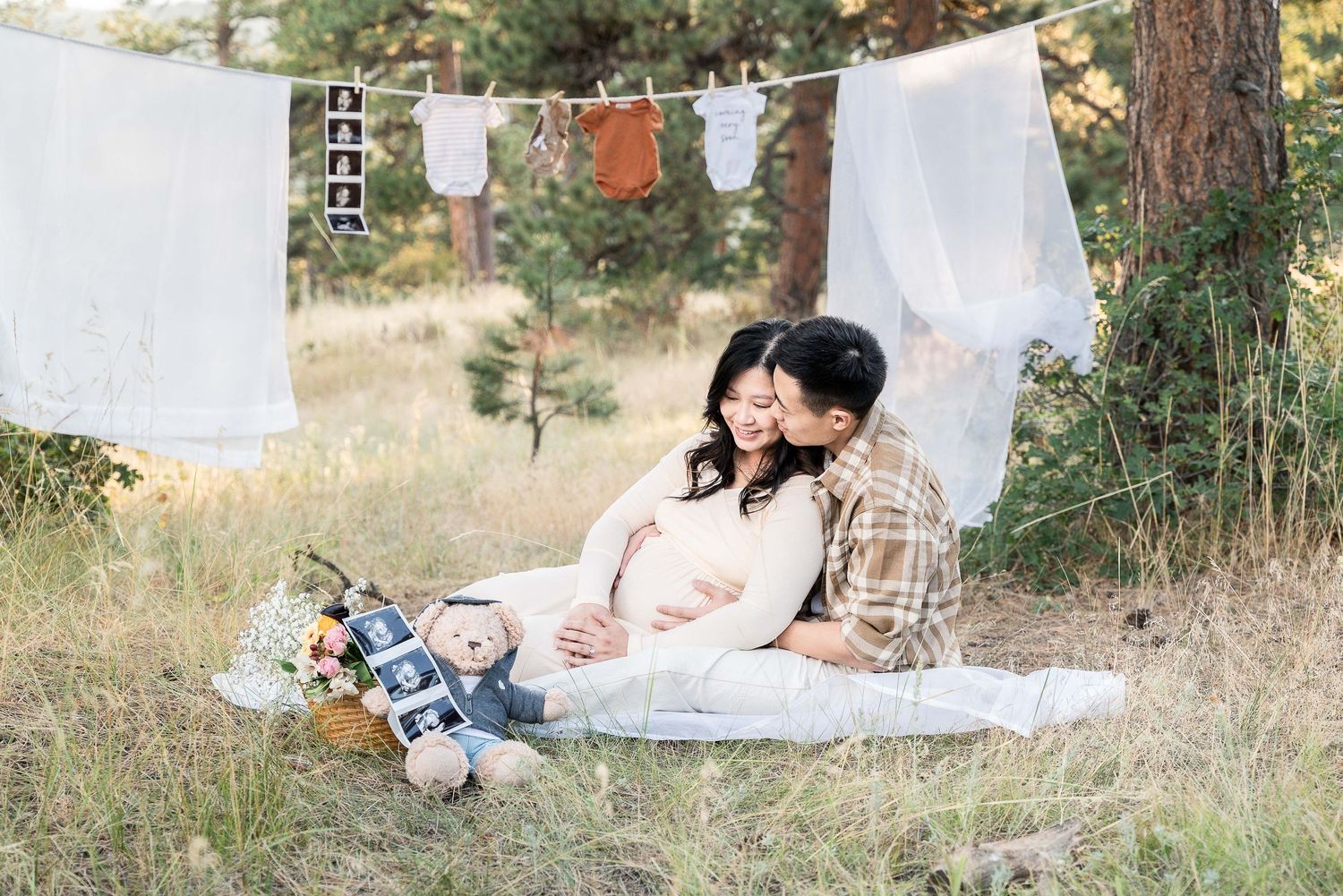 A romantic outdoor picnic setup with white fabric draping, pillows, and a rustic basket in a sunlit meadow.
