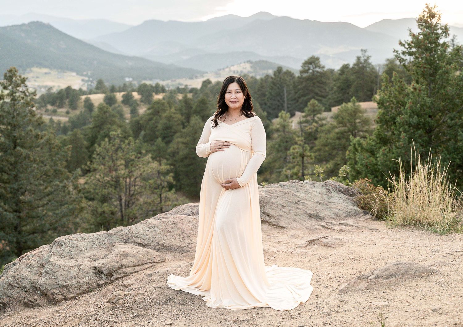 A scenic maternity photo session captured on a rocky mountain overlook with sweeping mountain vistas in the background.