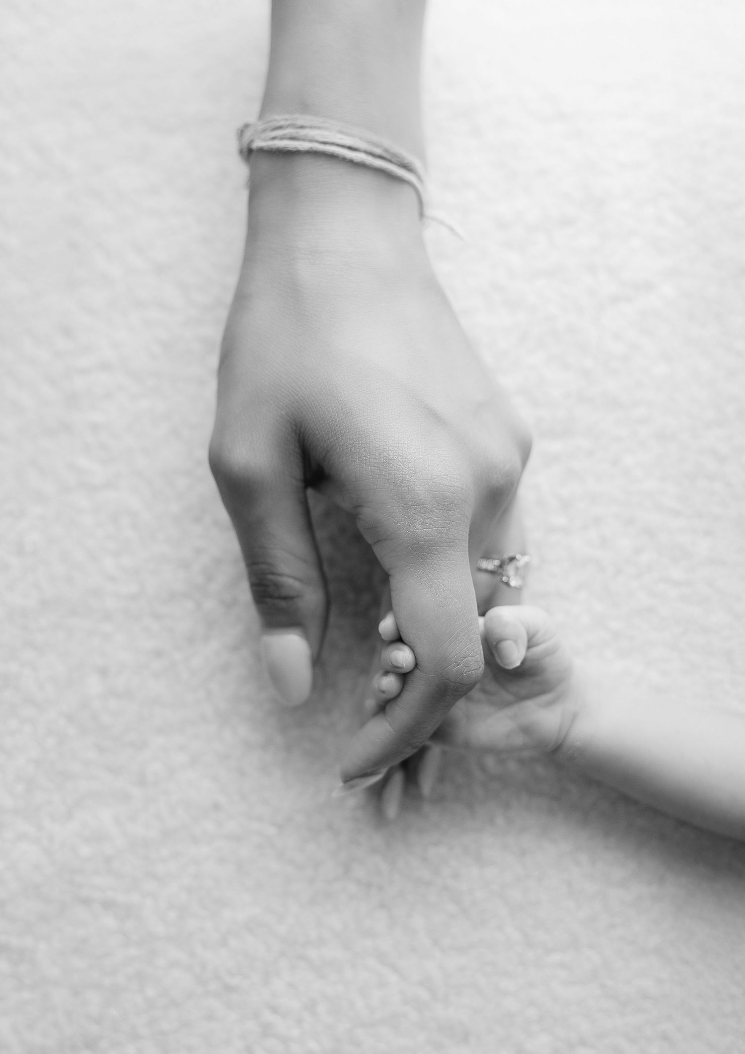 A tender moment captured in black and white showing an adult hand holding a tiny baby hand with a bracelet visible.
