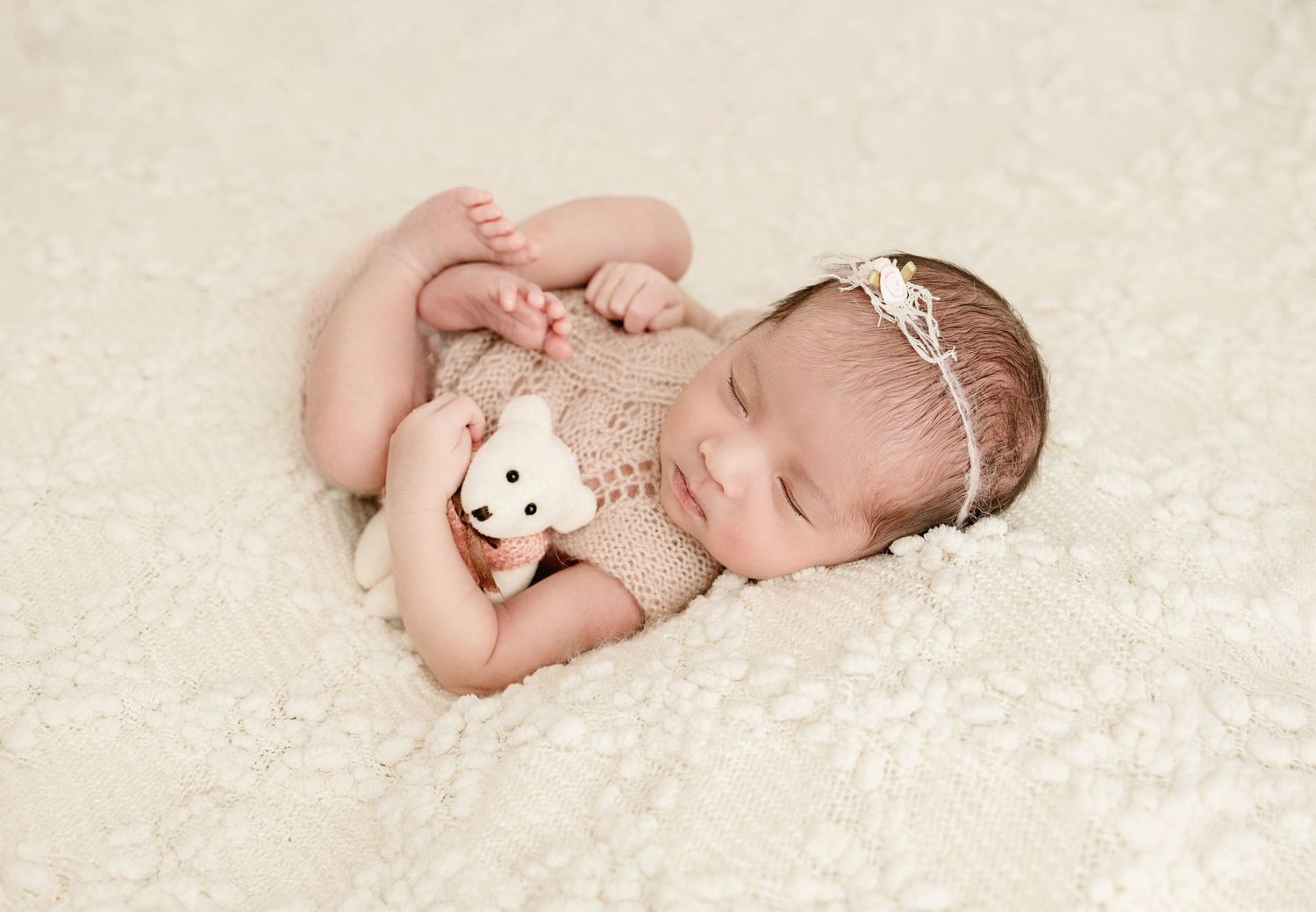 A series of connected newborn baby photos showing peaceful sleeping poses on soft white fabric with a small stuffed animal.