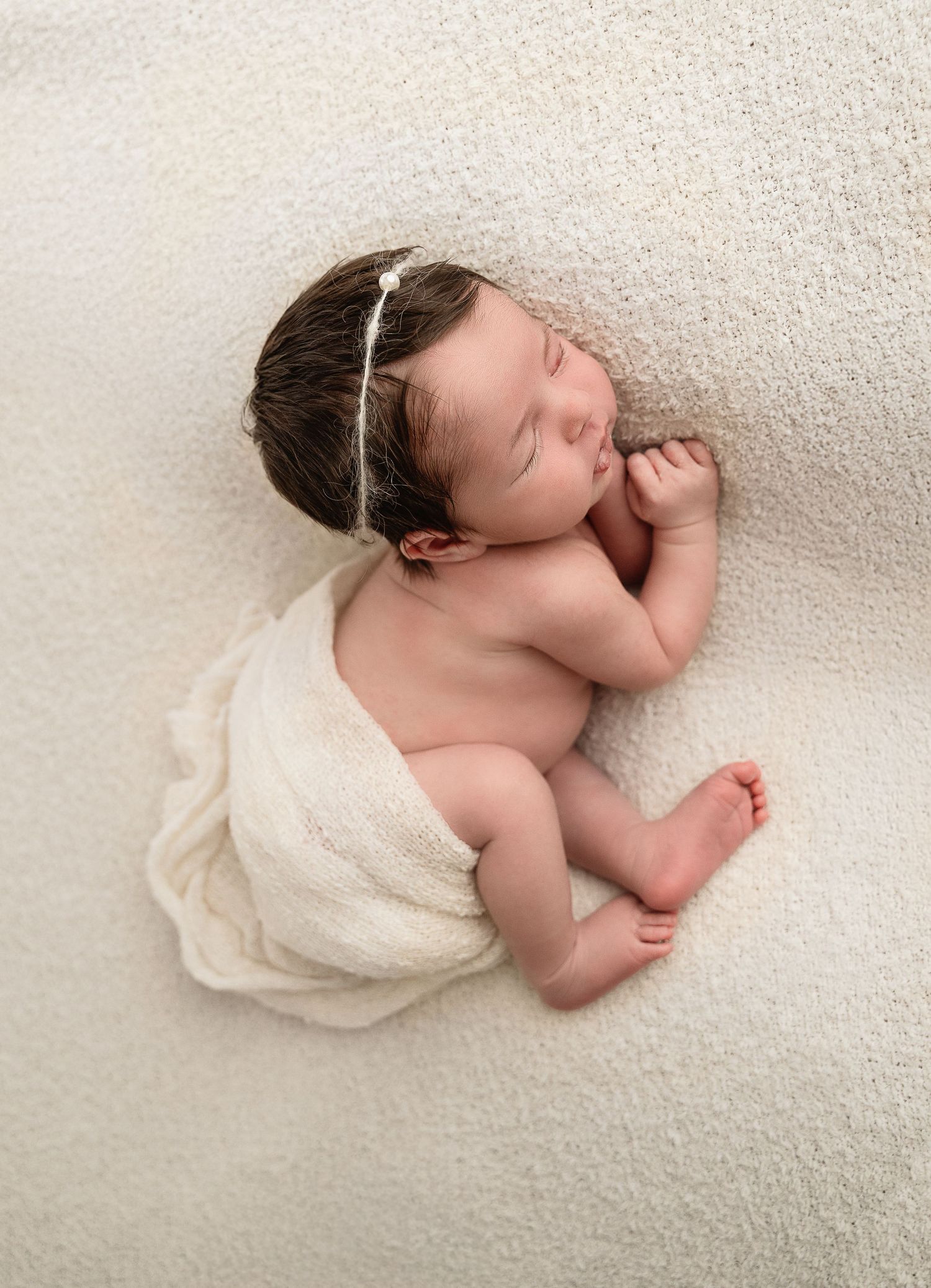 Peaceful sleeping newborn wrapped in white cloth against textured background.