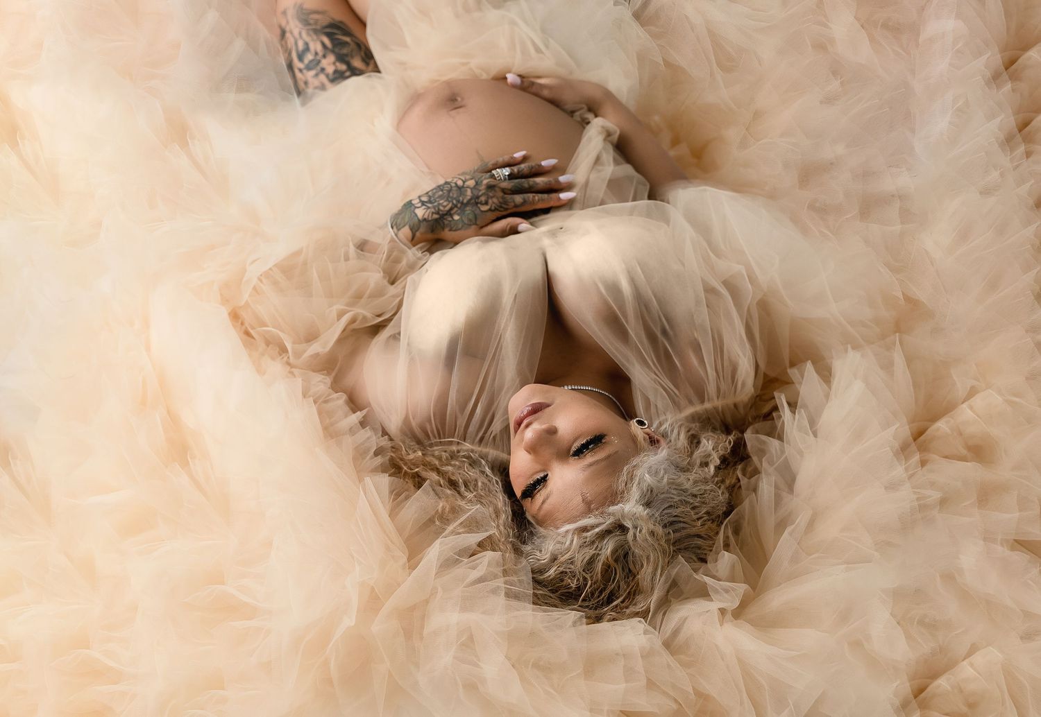 Dreamy maternity portrait surrounded by flowing tulle fabric in cream tones.