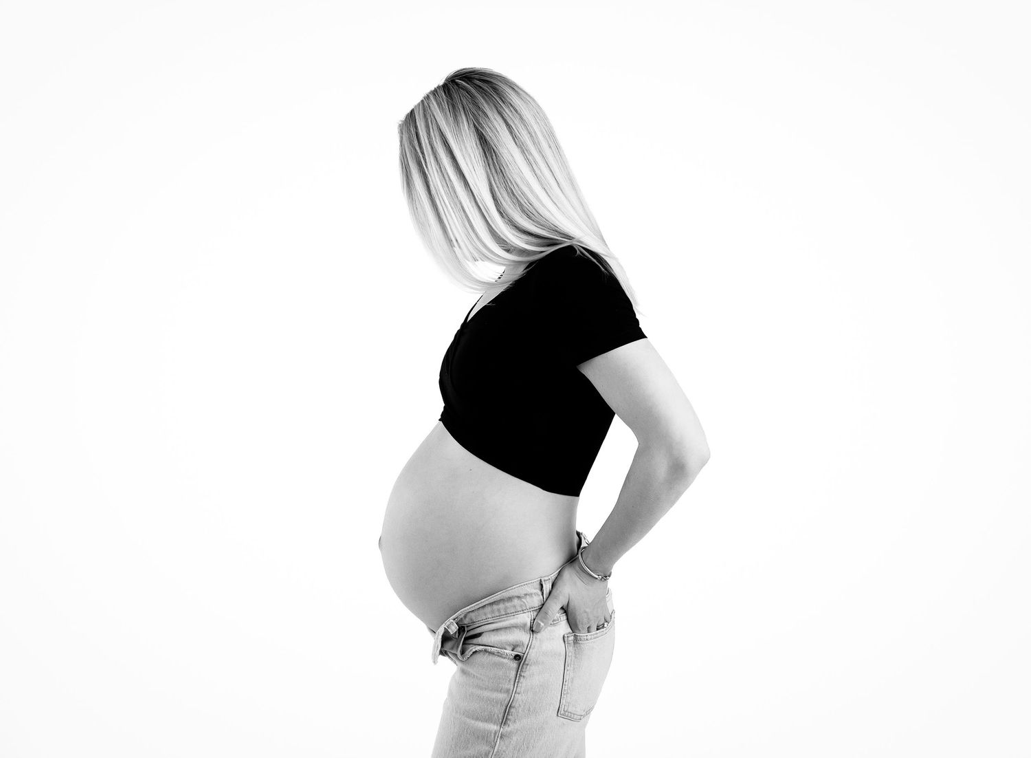 Black and white photo of a pregnant woman in a black crop top and jeans, showing her baby bump.