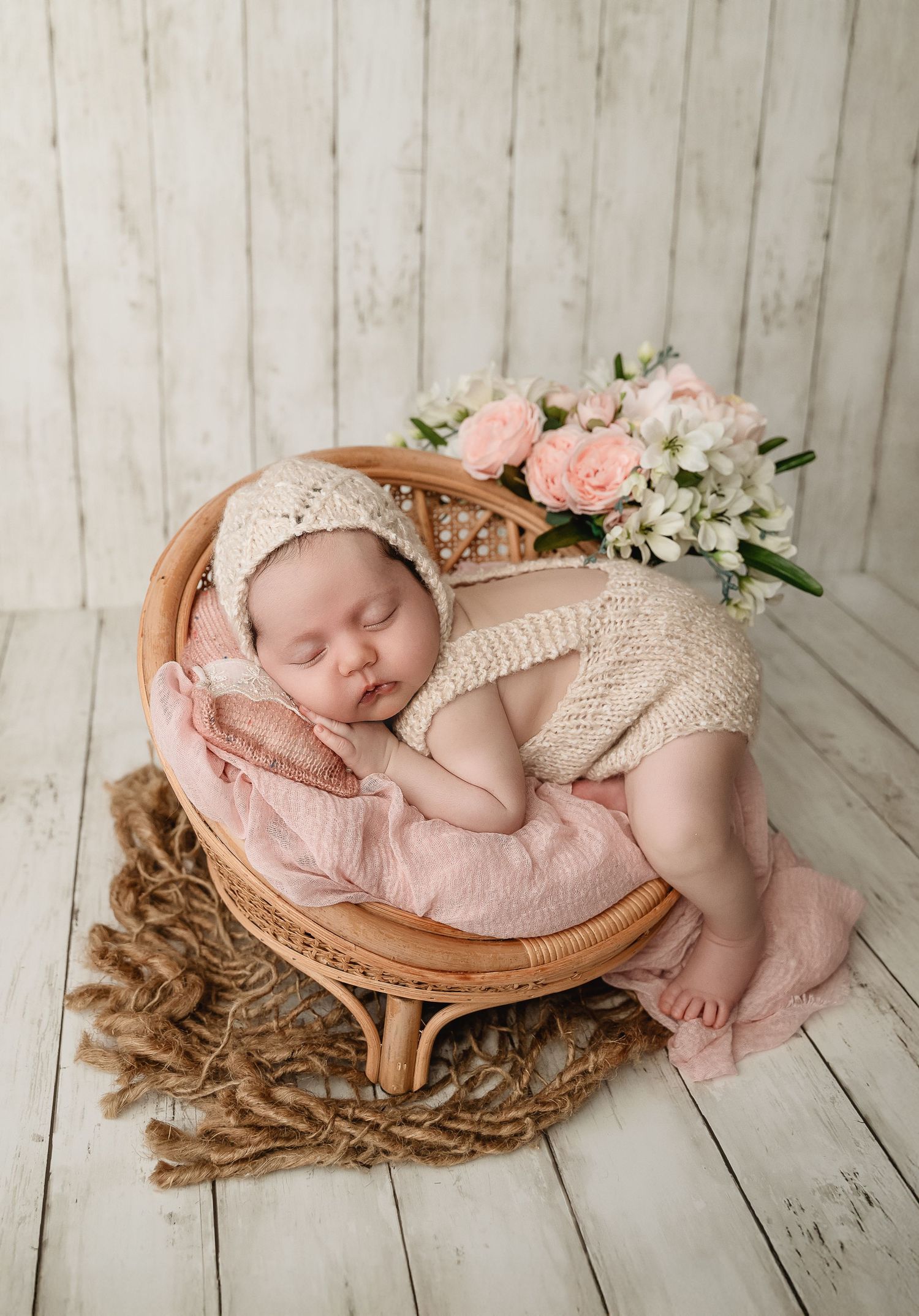 Newborn photography setup with pink floral accents and wooden vintage chair.