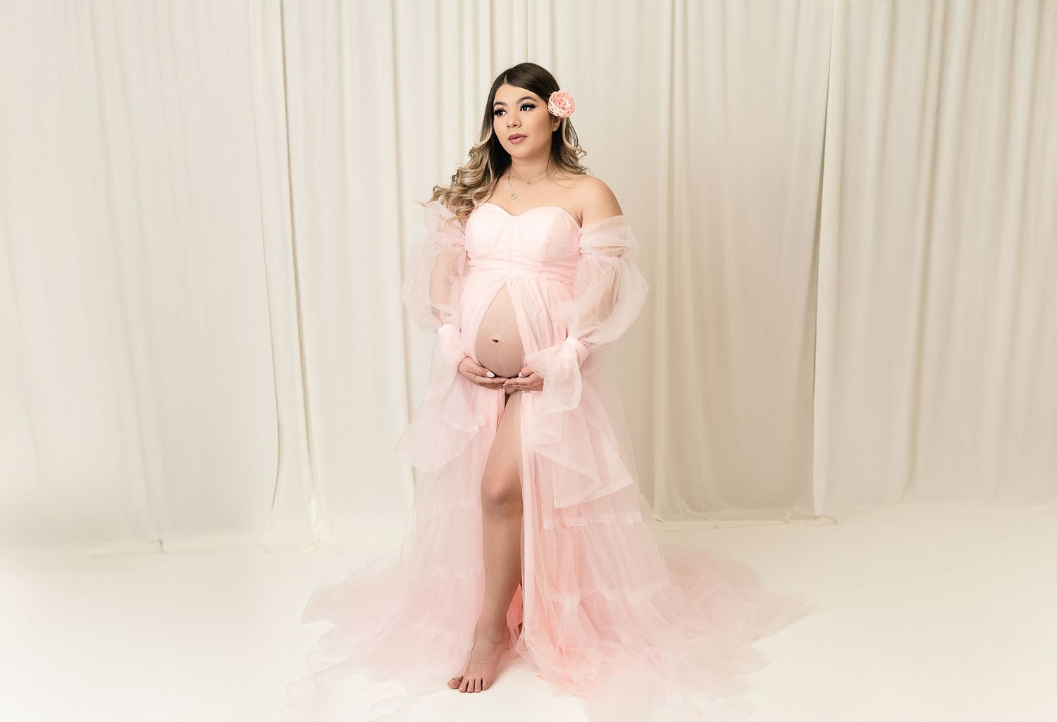 Maternity photo of a flowing pink tulle gown against a white backdrop.