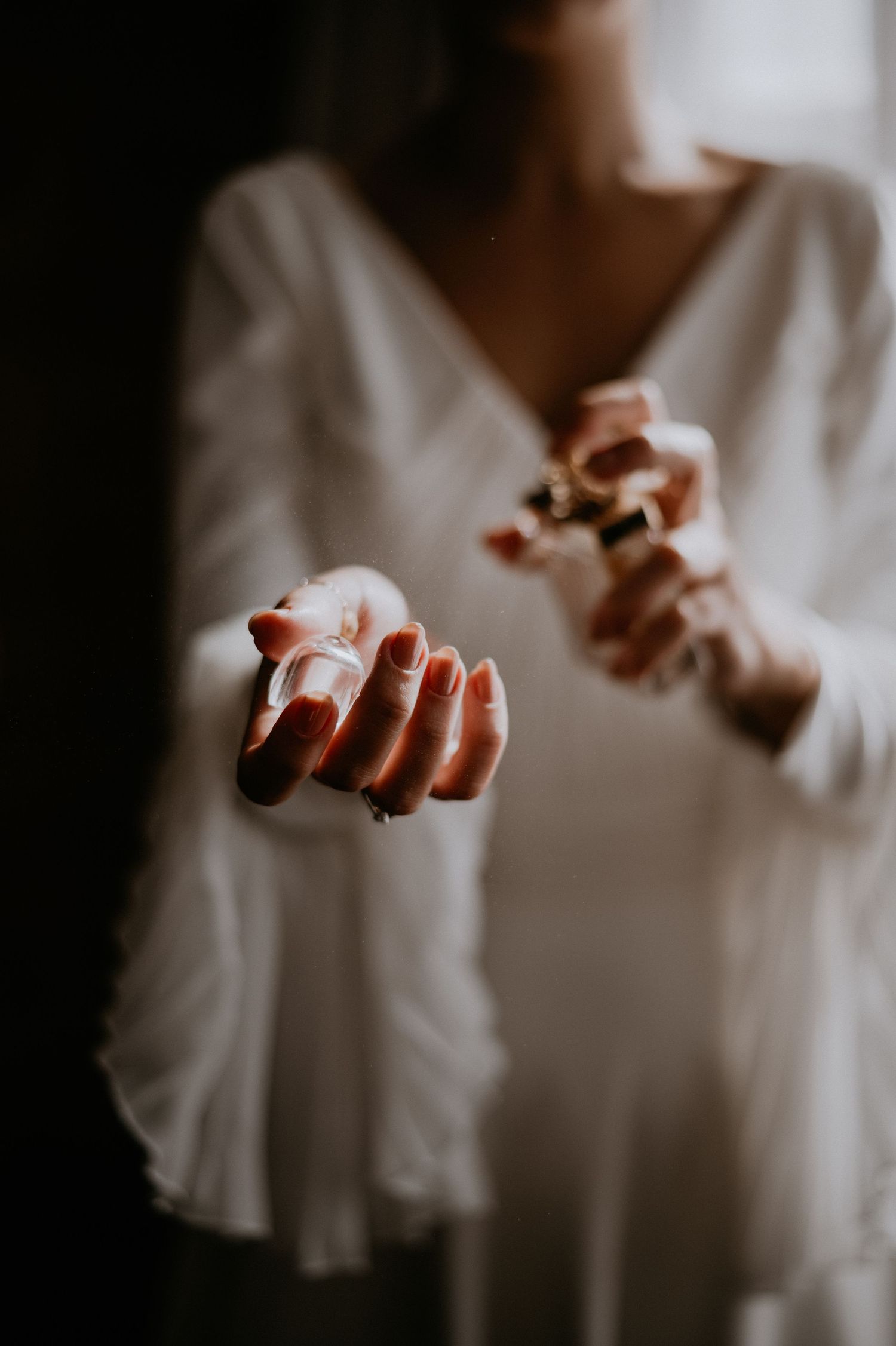 Artistic close-up of hands in soft light wearing a white long-sleeved dress.