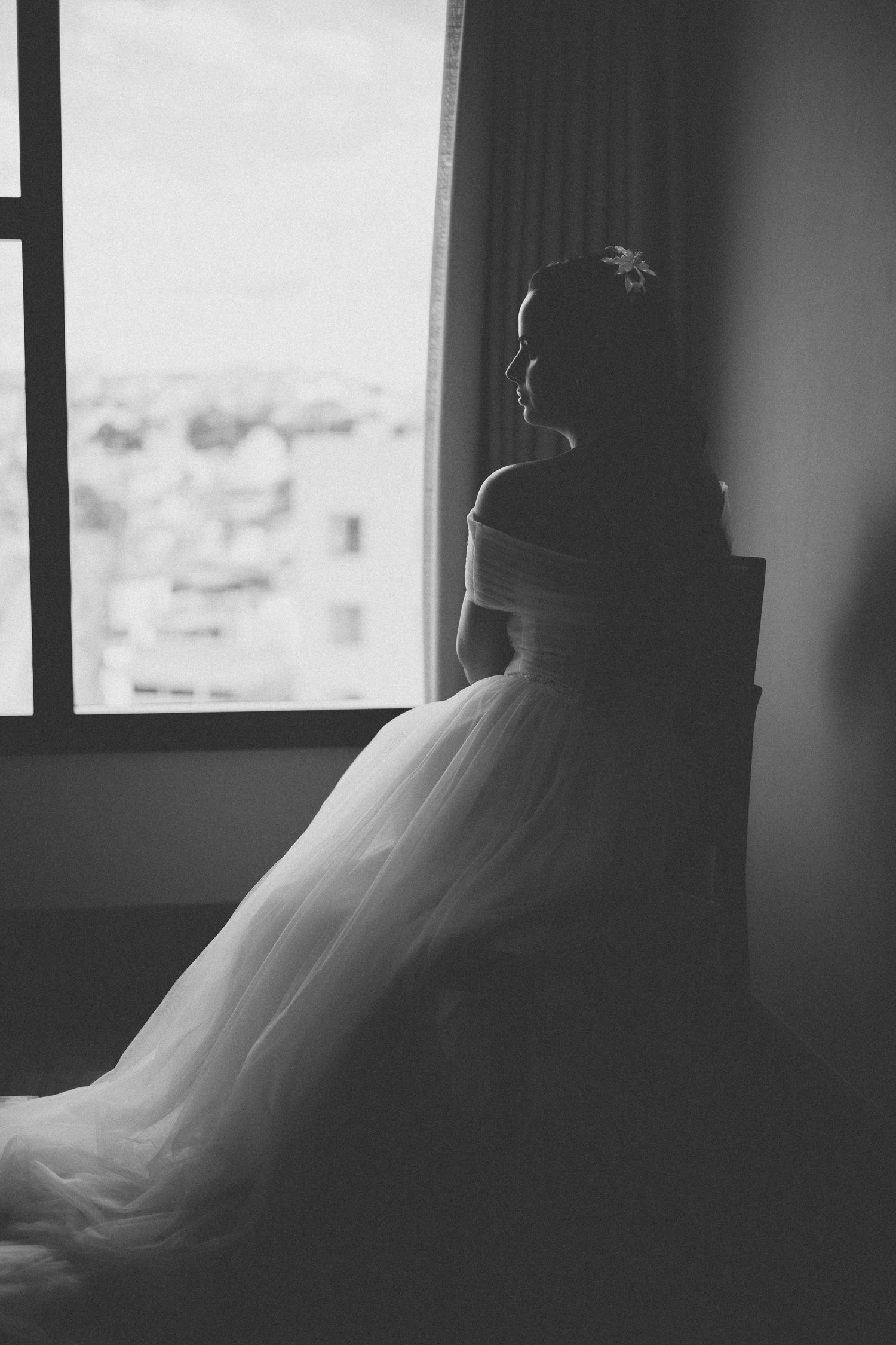Silhouette of someone in a wedding dress gazing out a window in black and white.