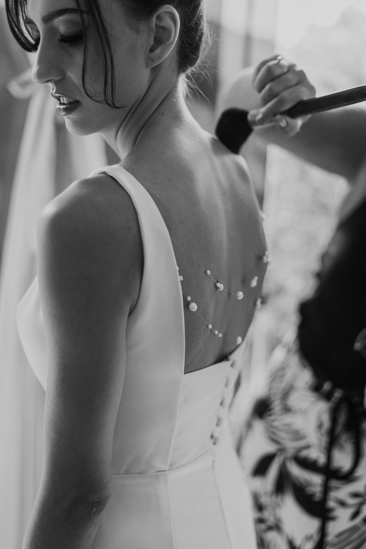 Black and white image of a bride's back showing delicate button details while getting ready.