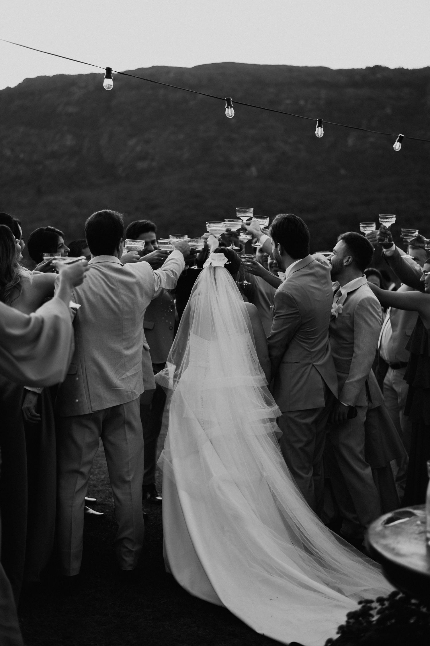 Wedding guests gather around long trailing veil at outdoor mountain reception.
