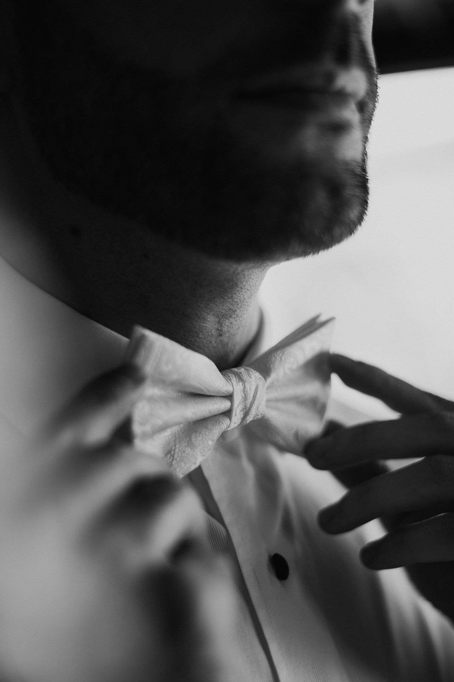 Black and white close-up of adjusting bow tie with formal attire.