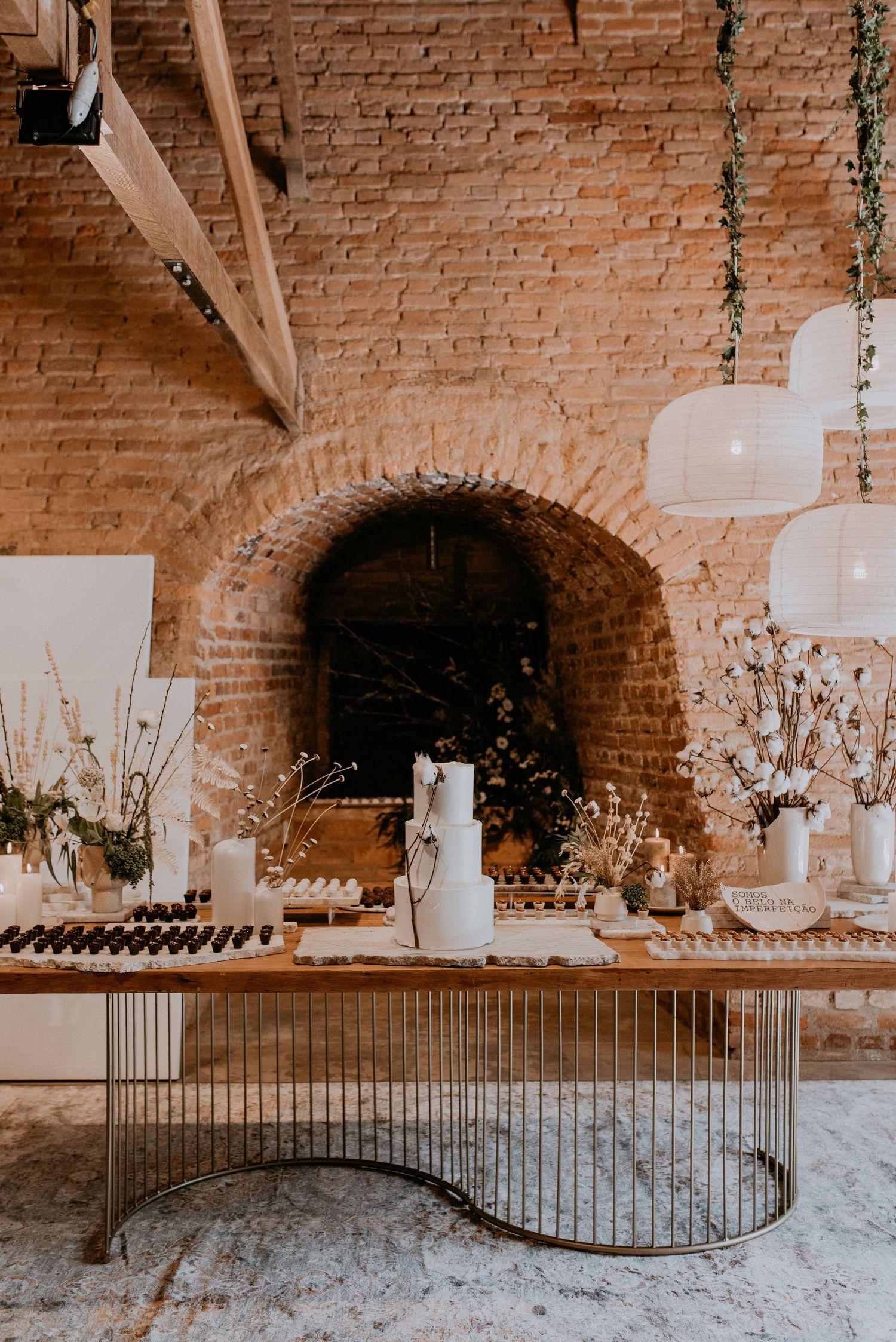 Elegant dessert display table with white florals against exposed brick wall and arched alcove.