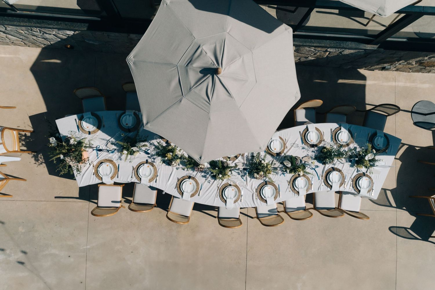 A white umbrella casting shadows over a row of wedding party shoes arranged outdoors in perfect symmetry.