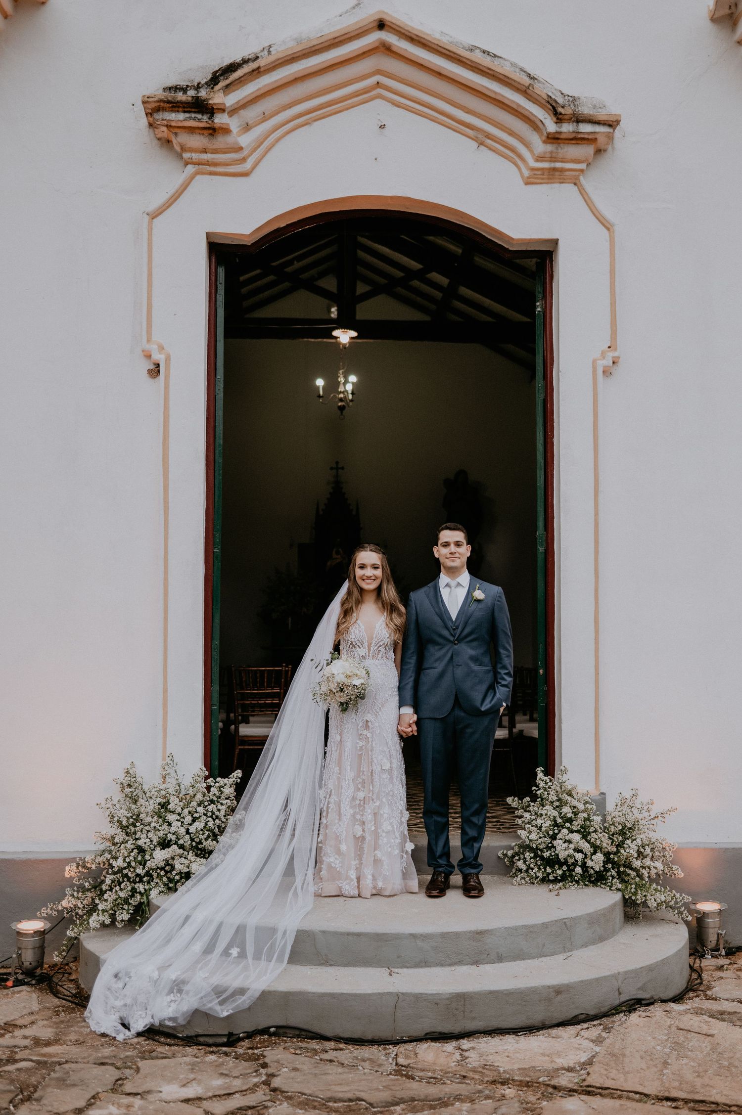 Newlyweds standing in church doorway decorated with white flowers.