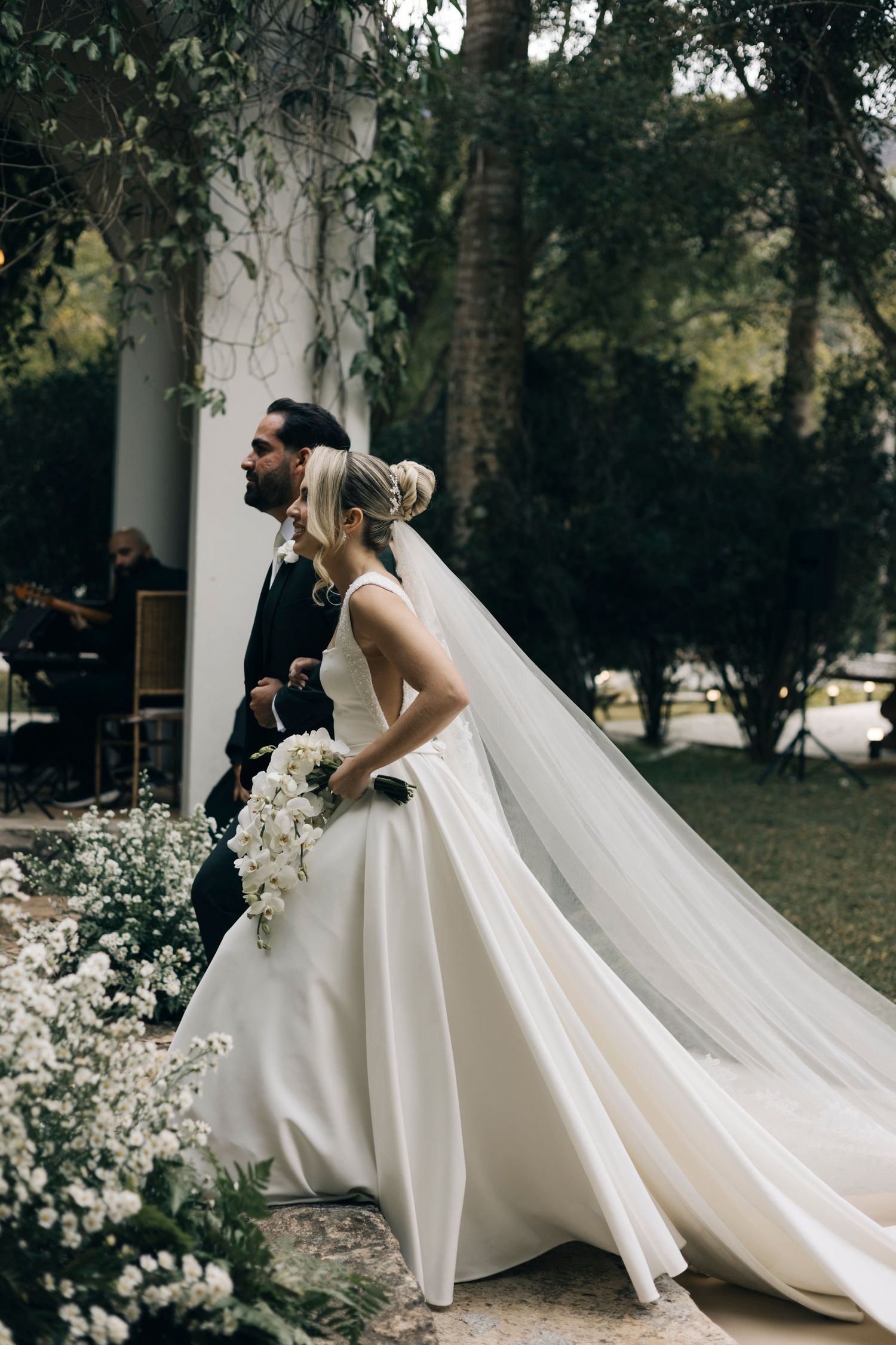 Elegant white wedding gown with flowing train captured in a romantic outdoor garden setting.
