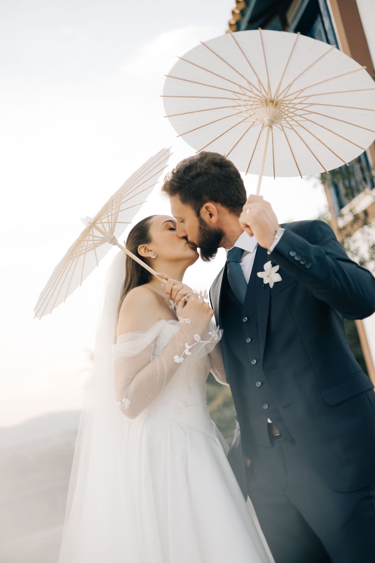 Romantic wedding moment under white parasols against an architectural backdrop.