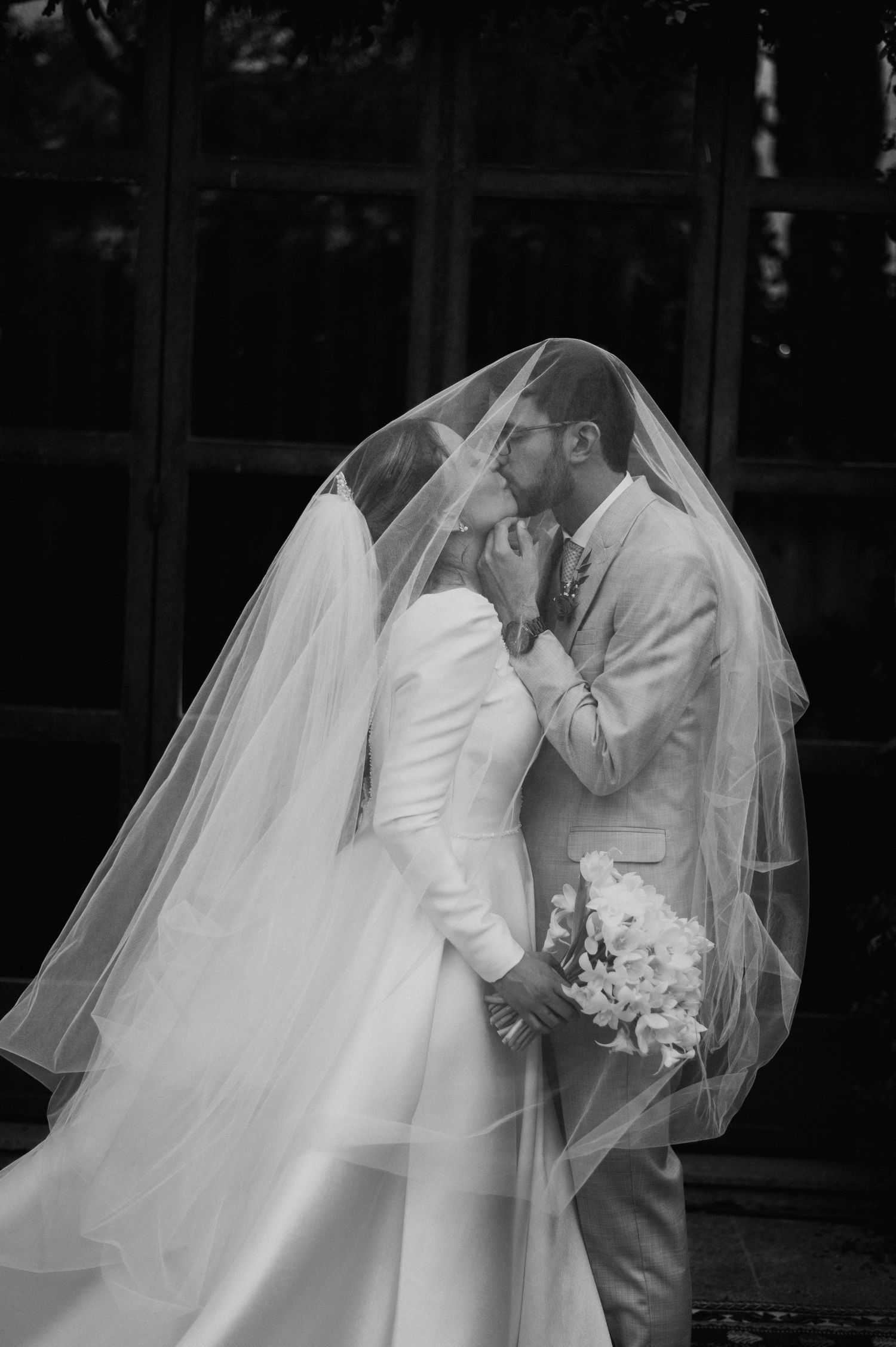 Romantic black and white photo of newlyweds sharing an intimate moment under a flowing veil.