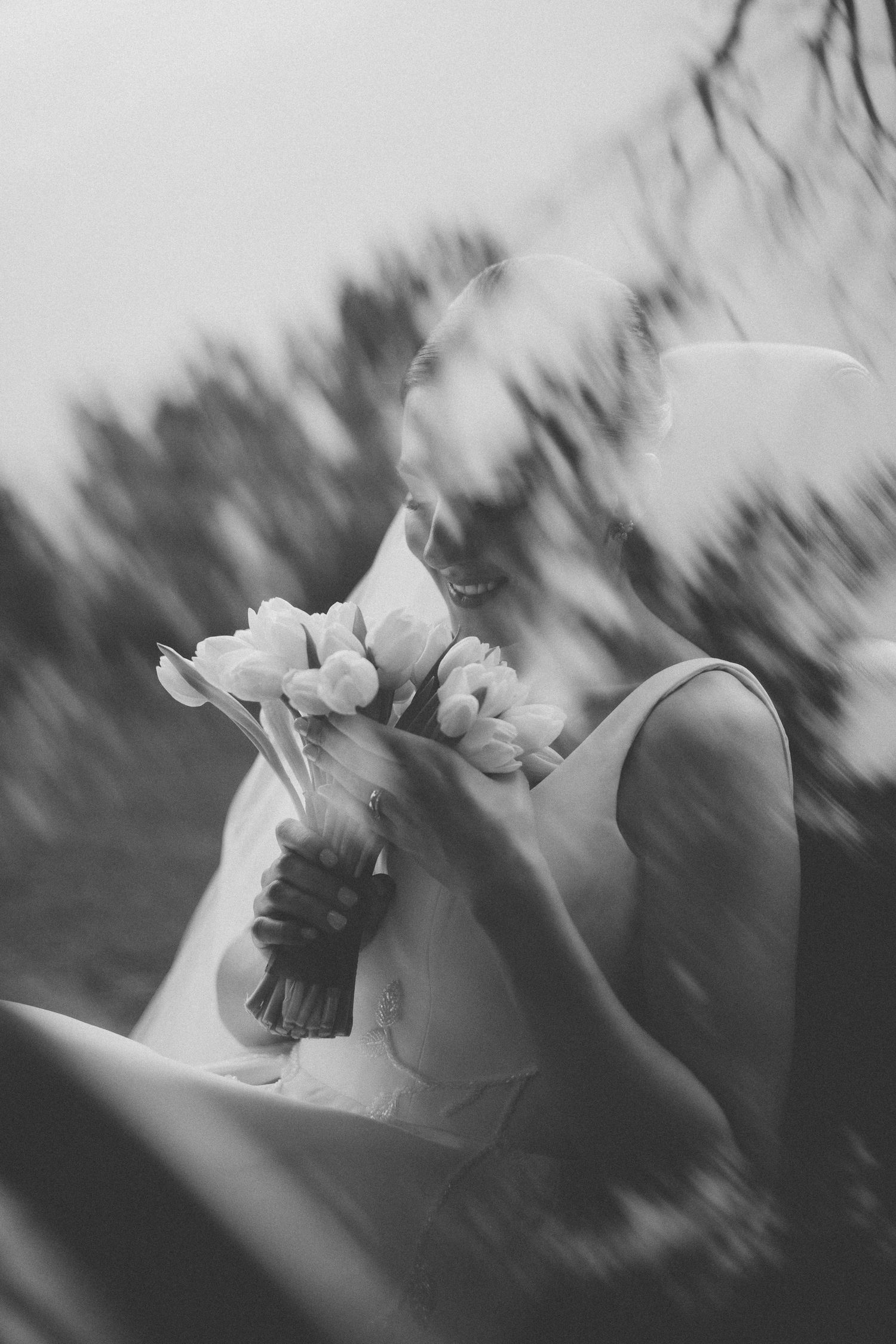 Artistic black and white photo of someone holding a delicate bouquet of tulips with blurred shadows in soft focus.