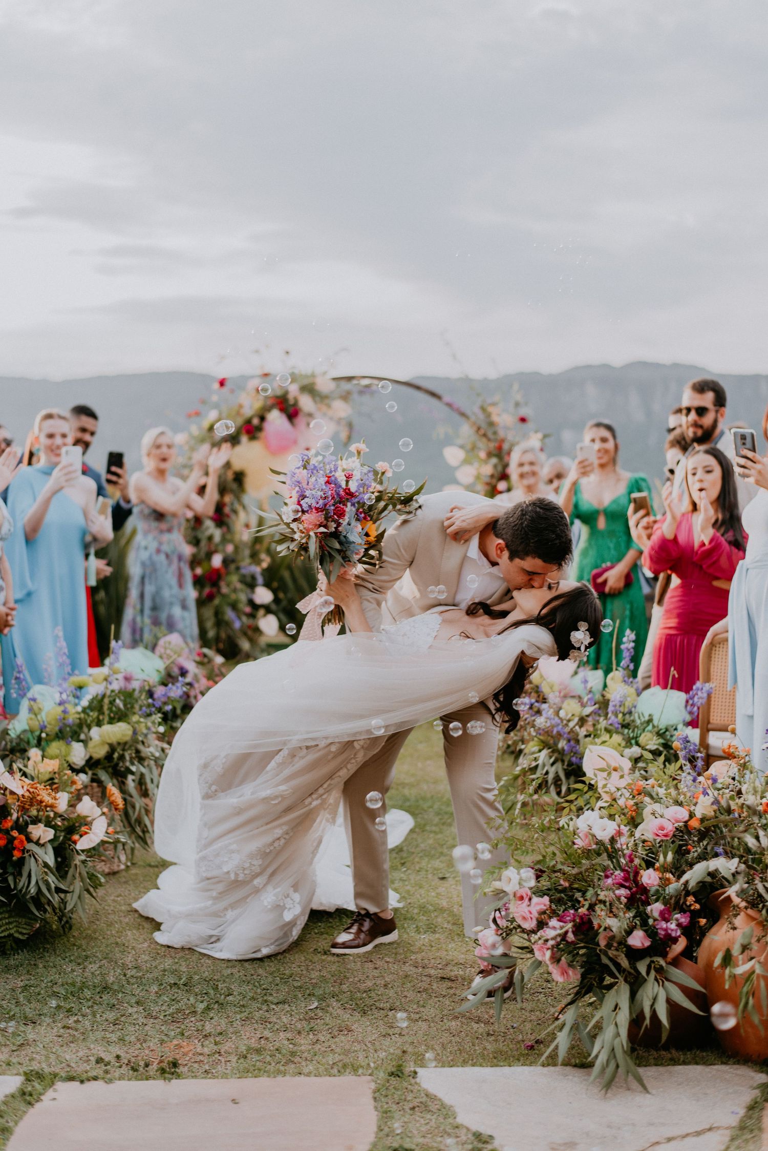 Romantic wedding ceremony moment under floral arch with mountain backdrop.