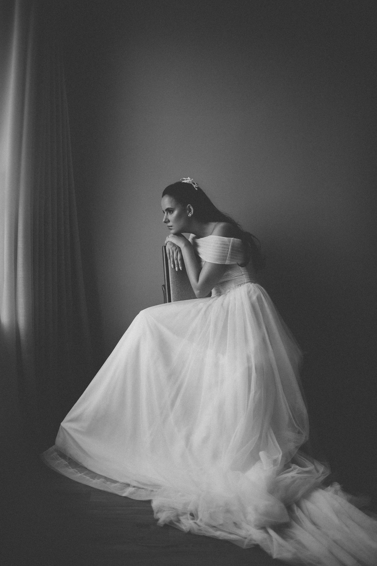 Dramatic black and white portrait of a wedding dress against a dark background.