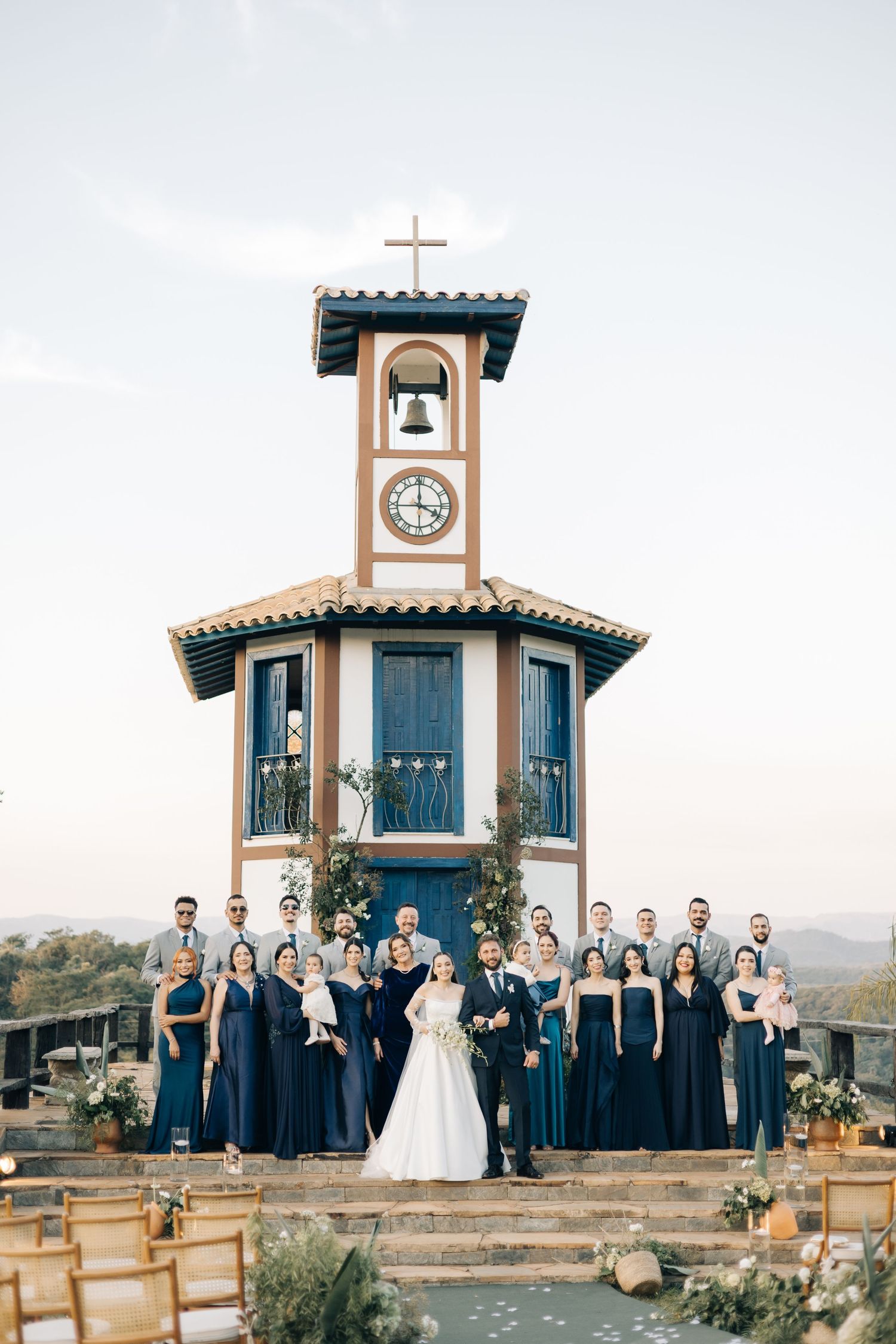 Wedding party in navy blue attire posed in front of a charming chapel with a clock tower.