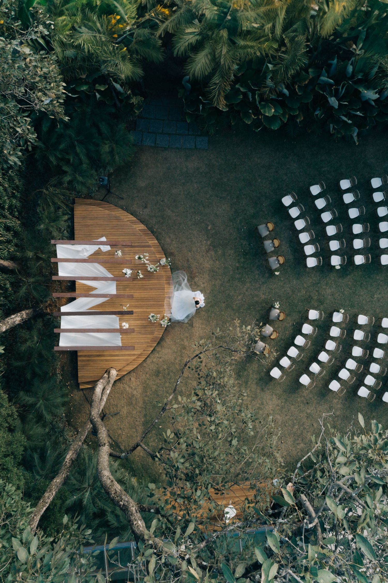 Aerial view of an outdoor wedding ceremony setup with white chairs arranged in curved rows and a wooden deck stage.