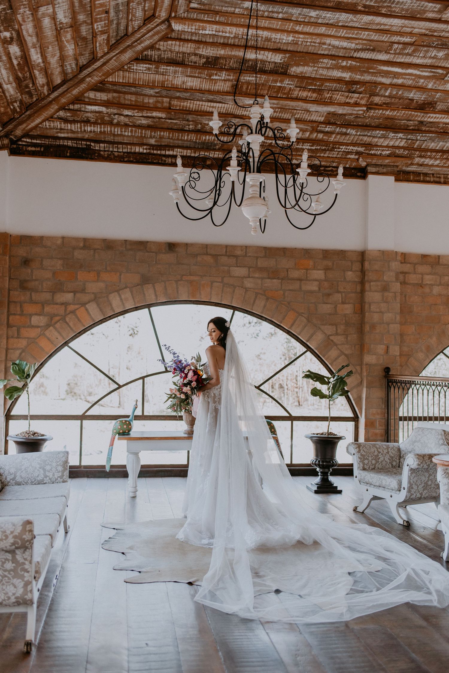 Dramatic full-length shot of wedding dress with cathedral train in rustic venue with arched windows.