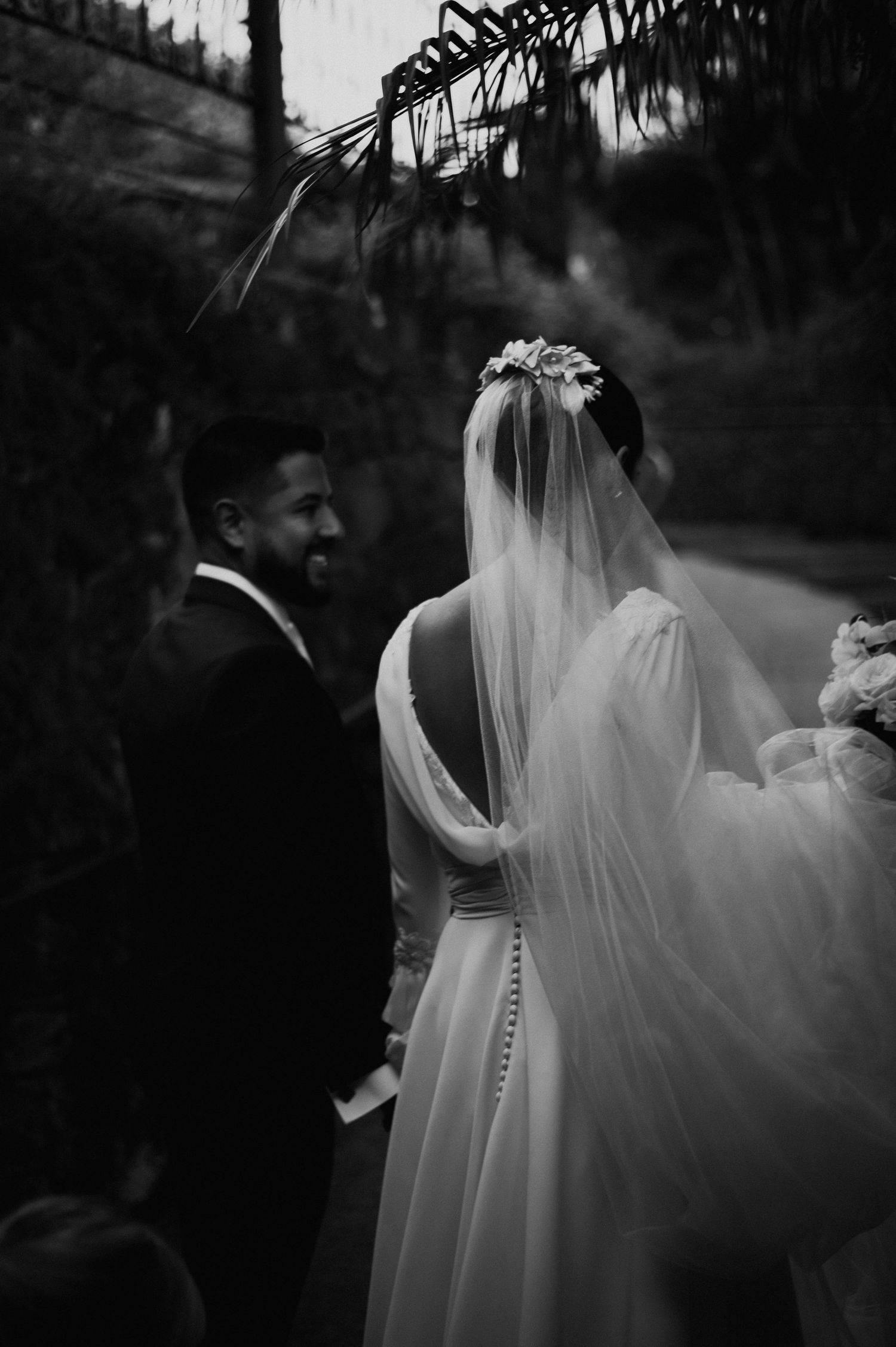 Black and white portrait of newlyweds sharing intimate moment under palm leaves.