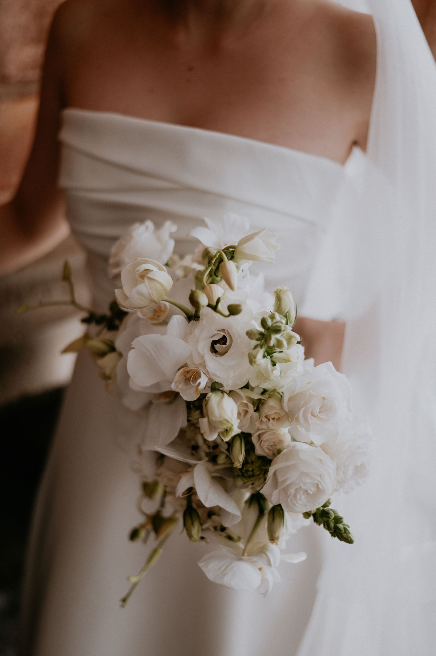 Close-up of elegant white rose and orchid bridal bouquet against wedding dress.